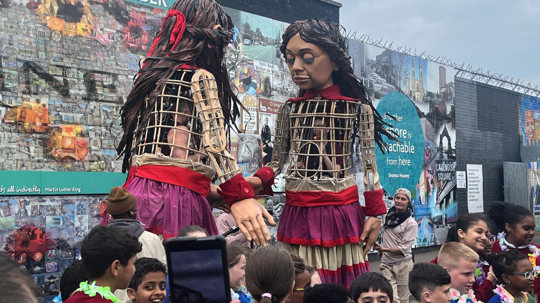 Little Amal, a 12ft (3.7m) puppet of a 10-year-old Syrian refugee, at the peace walls in west Belfast, as schoolchildren watch on