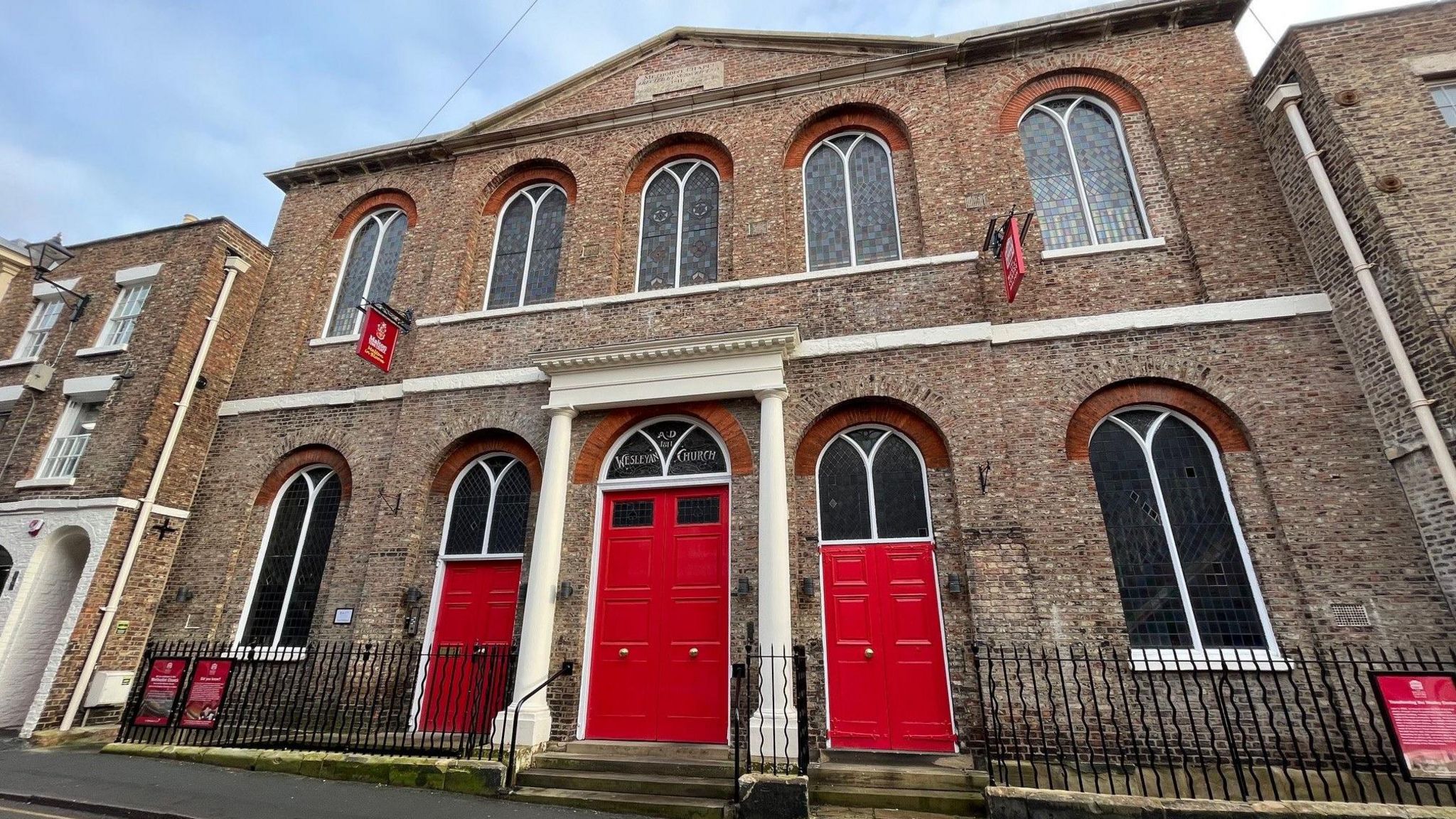 An image of The Wesley Centre. It is a traditional Methodist church style building with bright red doors 