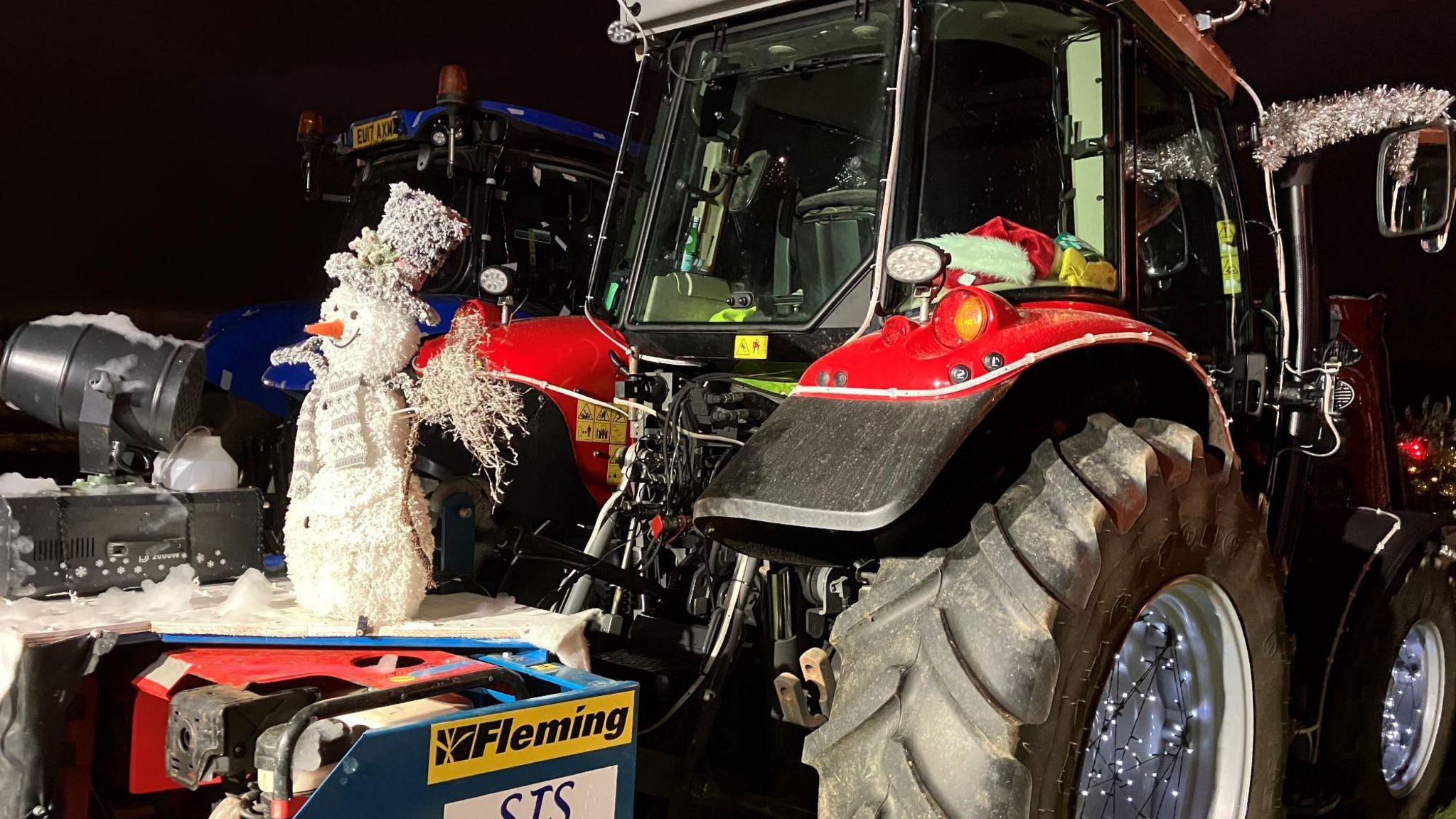Snowman sits at the from of a tractor decorated for Christmas 