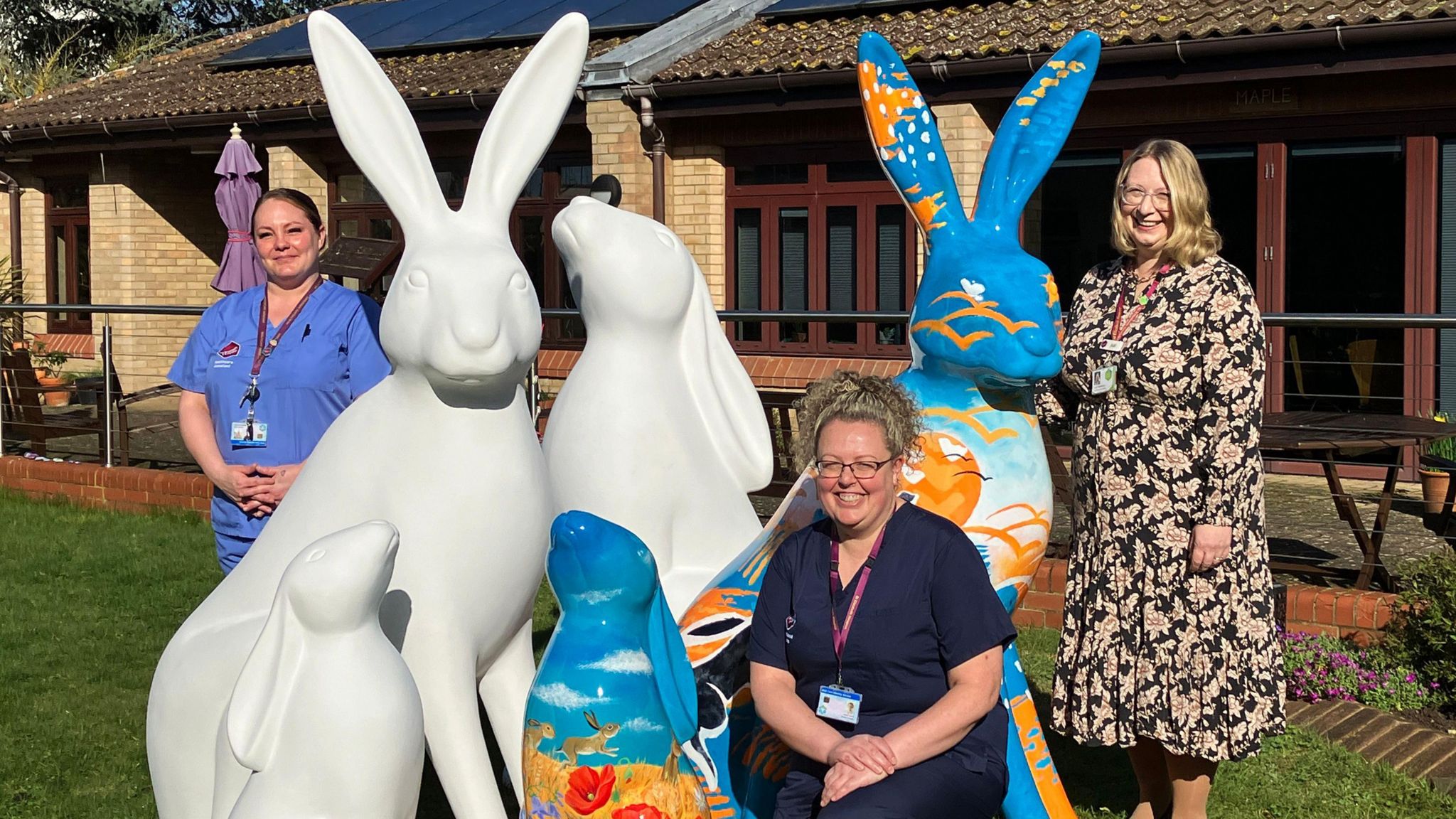 Three women stood with three white hare sculptures and two blue hare sculptures