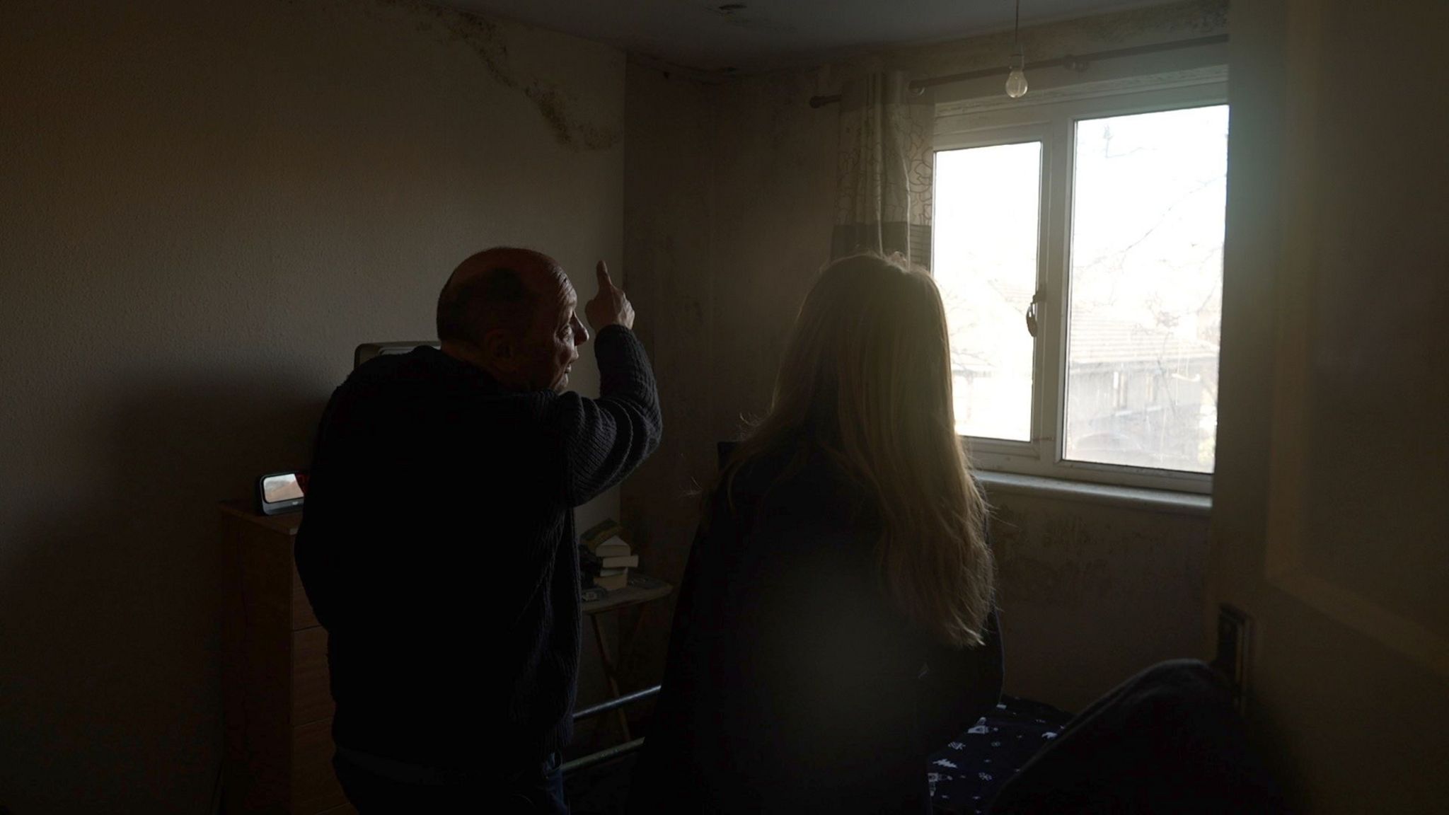 Man points to a damp and mouldy patch on the ceiling of his bedroom where water comes though when it rains