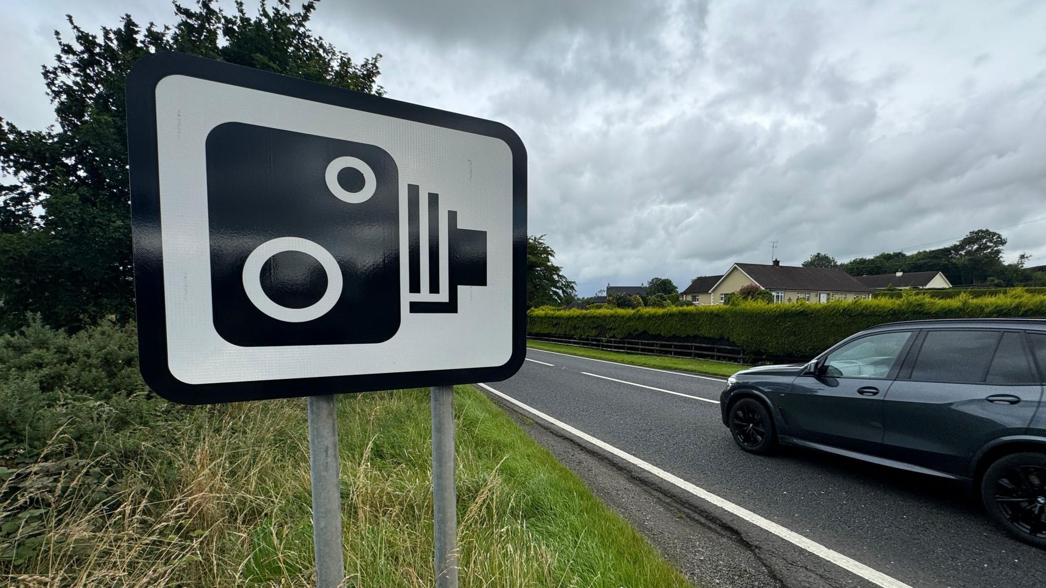 Image of a speed camera warning sign with a car driving past it. 