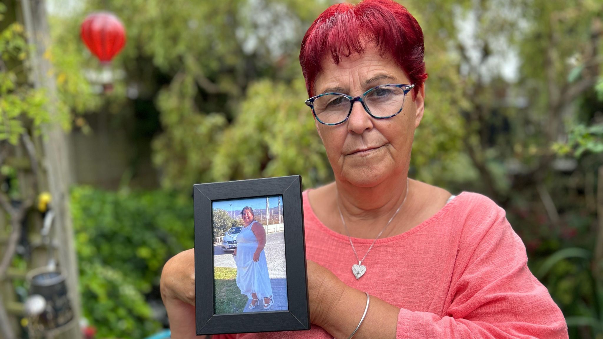 Woman in a salmon pink shirt holding up a picture frame with a woman pictured wearing a long white flowy dress