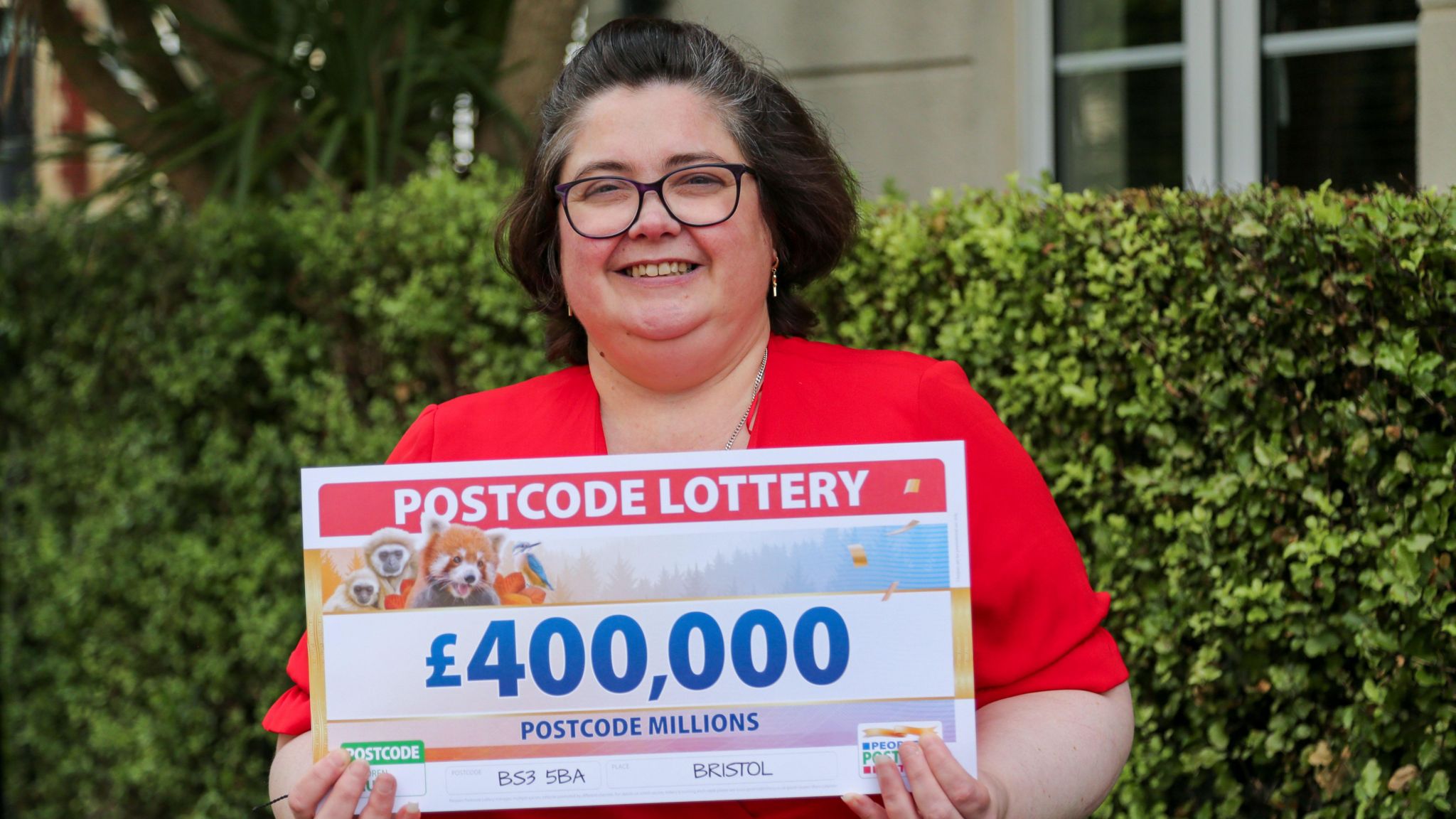 Karen McGlone wearing red top and holding a large £400,000 cheque outside her home. 