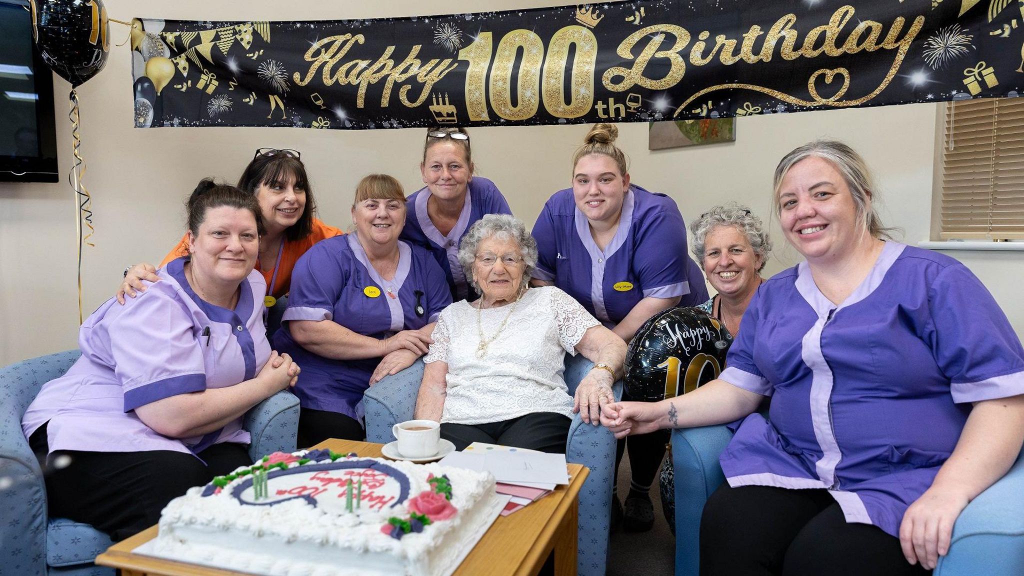 Bristol woman Joyce Weaver surrounded by care home staff under a banner wishing her a happy 100th birthday