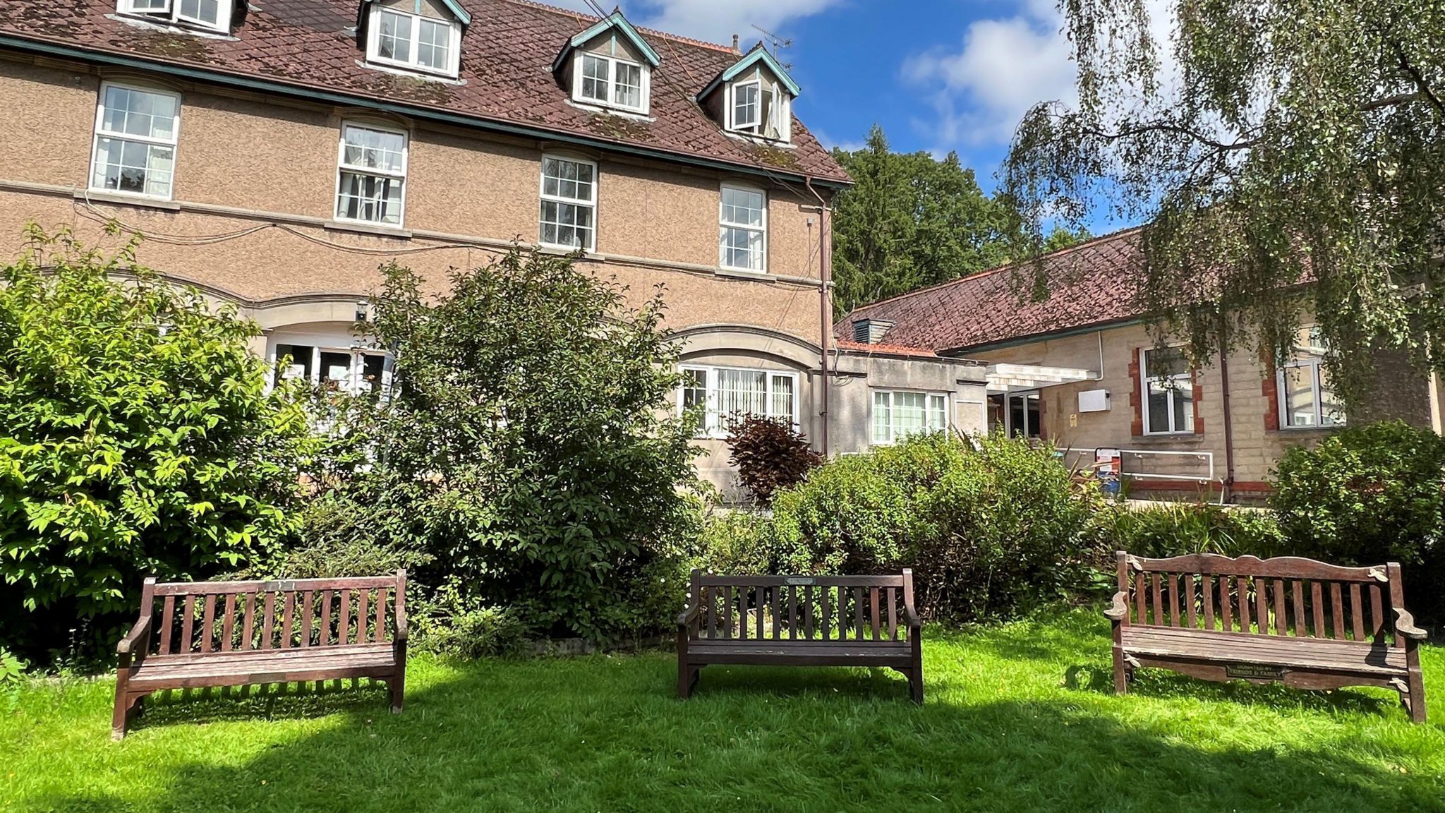 The garden at the Dilke Memorial Hospital with three benches on grass with buildings in the background