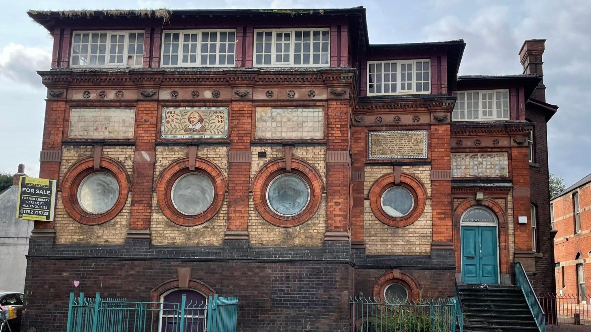 A picture of the former Stoke-on-Trent Library, designed by Charles Lynam in 1877

A red brick building with four circular windows with powder blue double doors