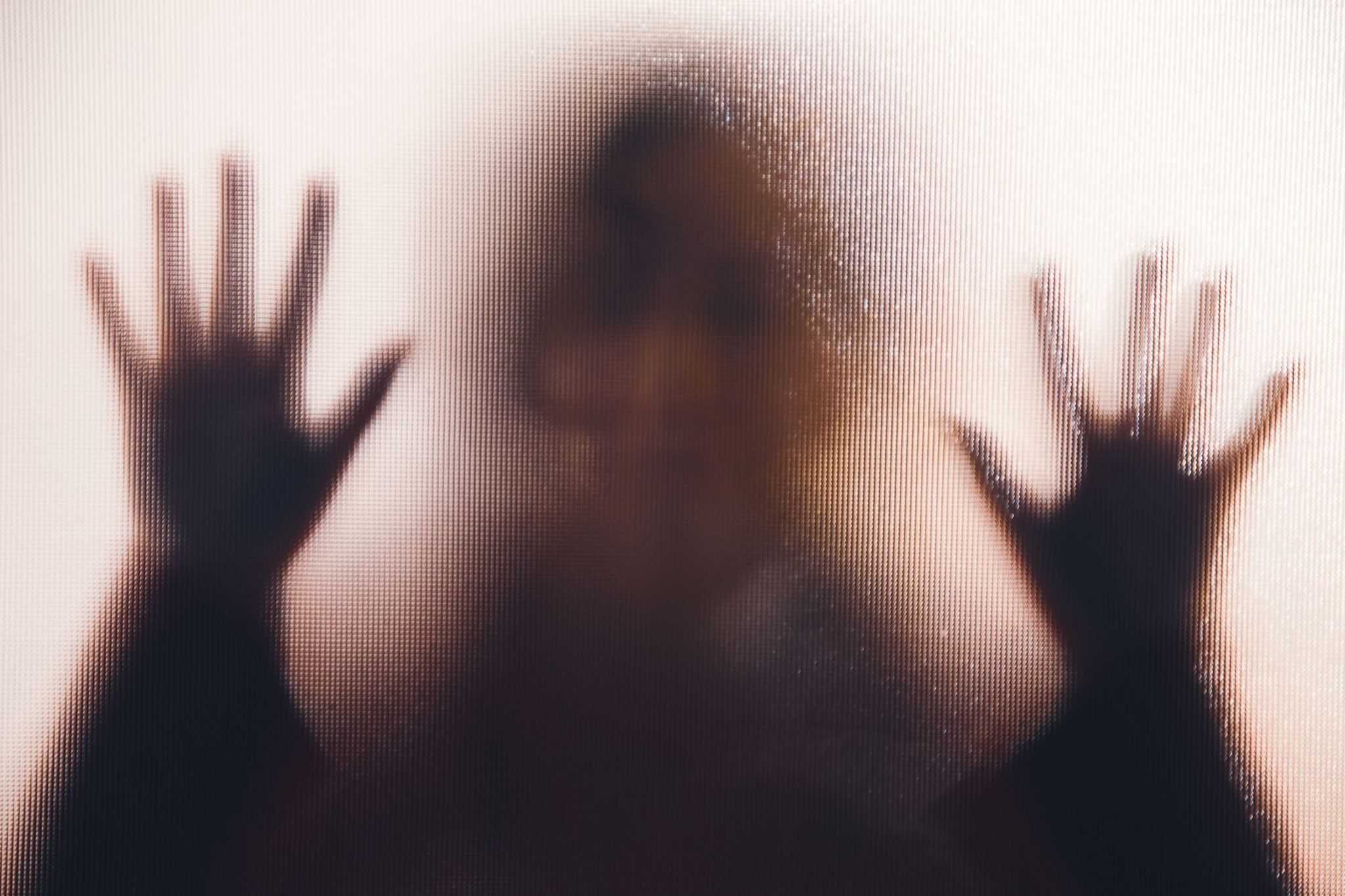 A woman's silhouette, her hands against a frosted glass window