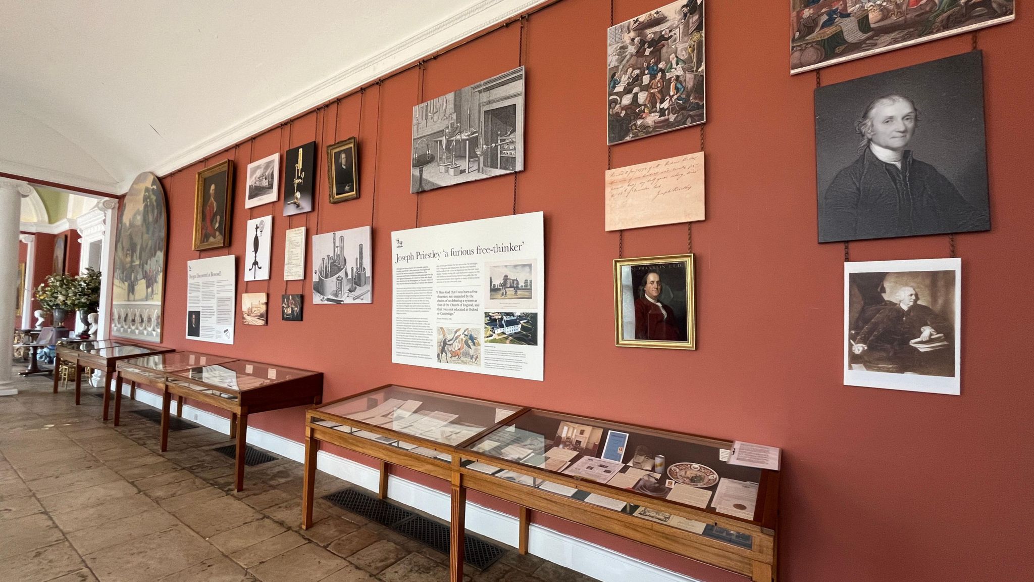 A wide corridor with stone floor, arched ceiling and display cabinets along the wall with pictures and information boards