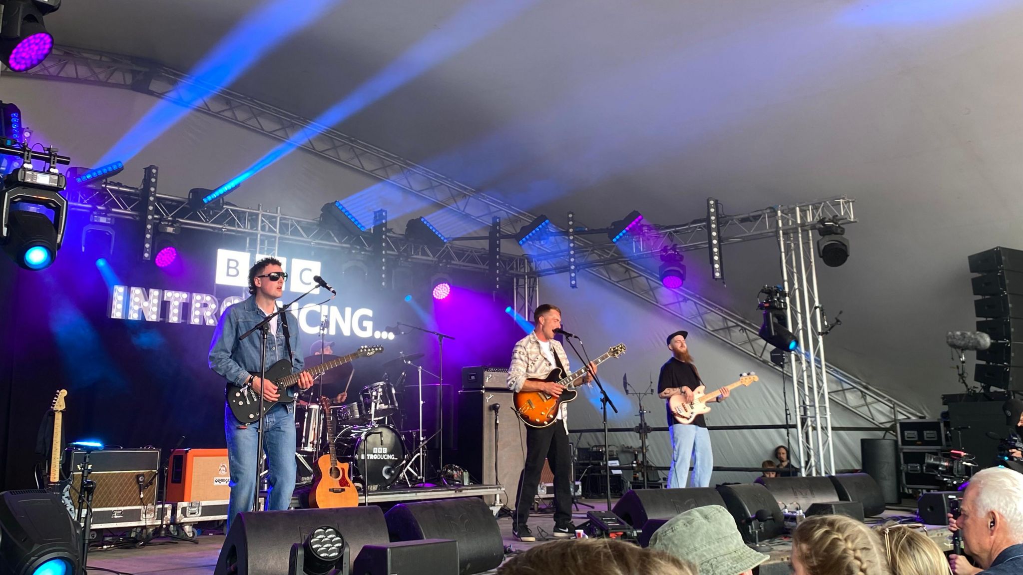 Sam Evans and his band performing on the BBC Introducing stage with the logo lit up behind them and a crowd watching near the front