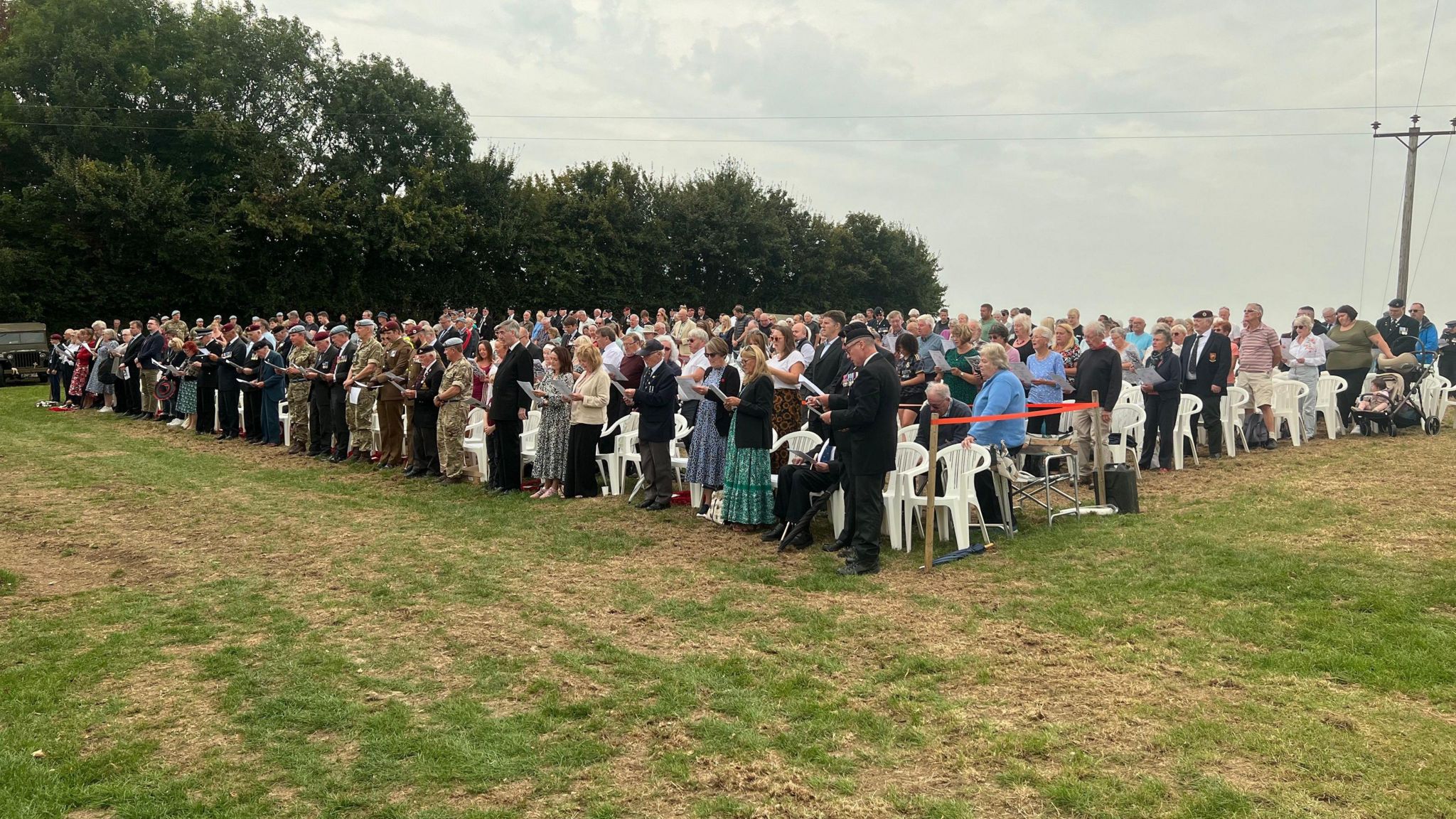 A large audience seated on white garden chairs.