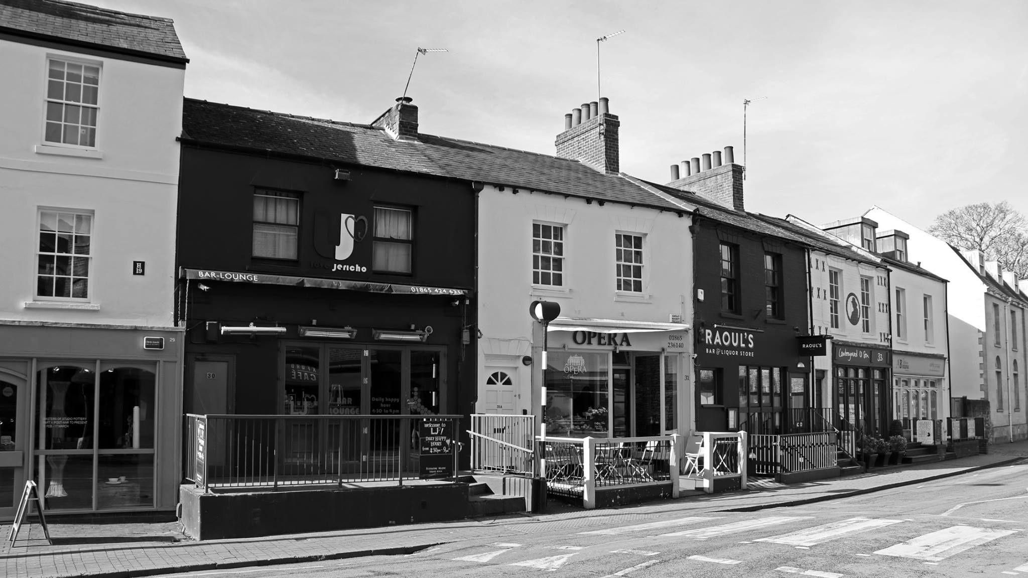 Walton Street shopfronts of Love Jericho bar, Opera Cafe, Raoul's bar and liquor store at one of the street's zebra crossings. This image is in black and white
