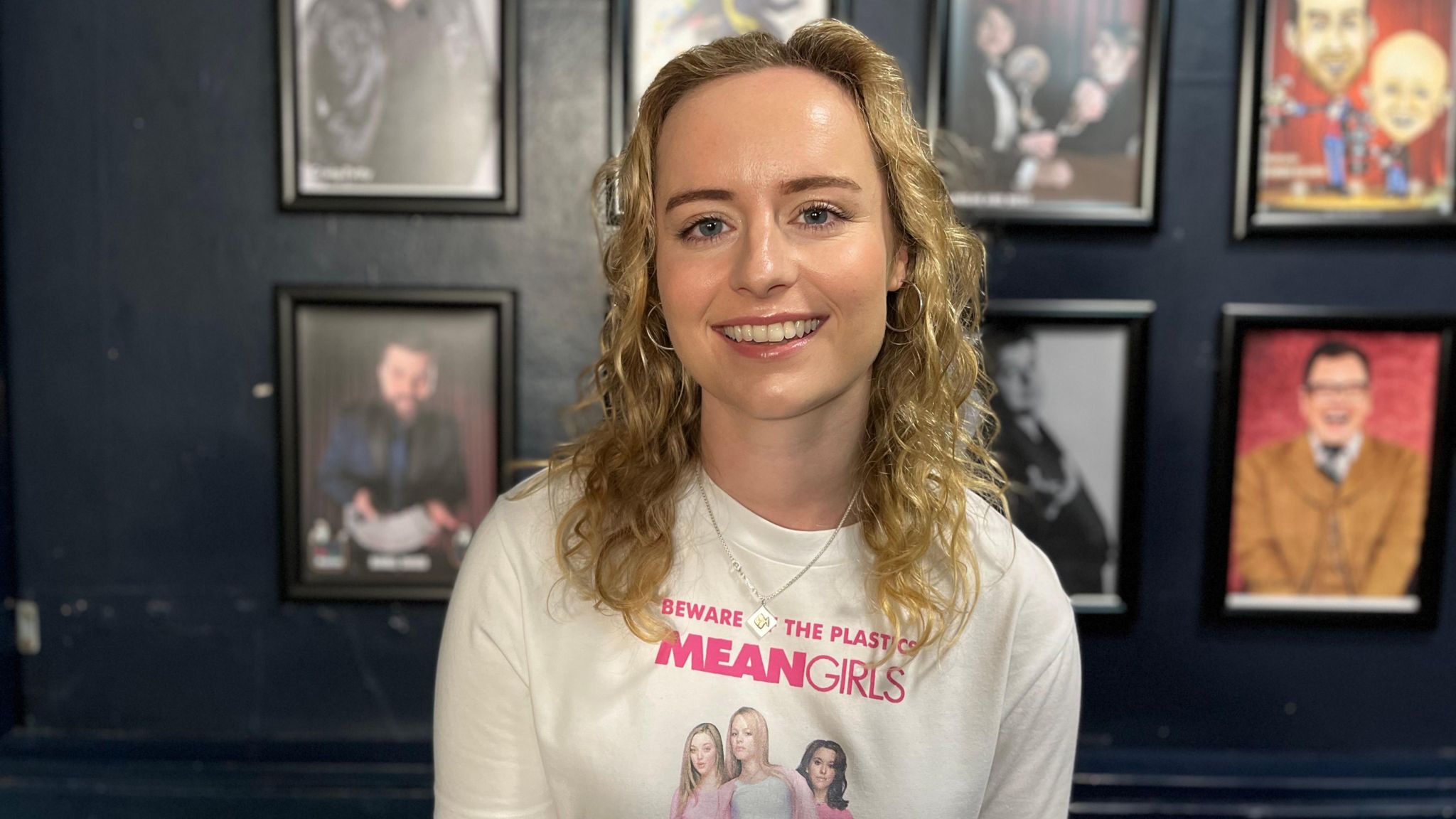 Dani Johns, smiling, wearing a white top that says 'beware of the Mean Girls' on it