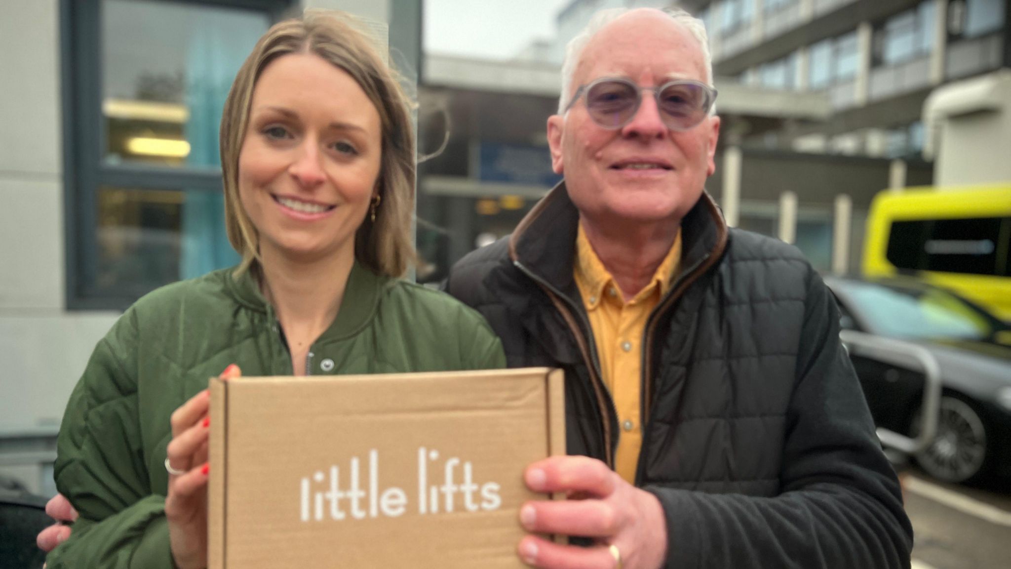 Oa and Graham standing outside Addenbrooke's hospital together holding a Little Lifts cardboard gift box