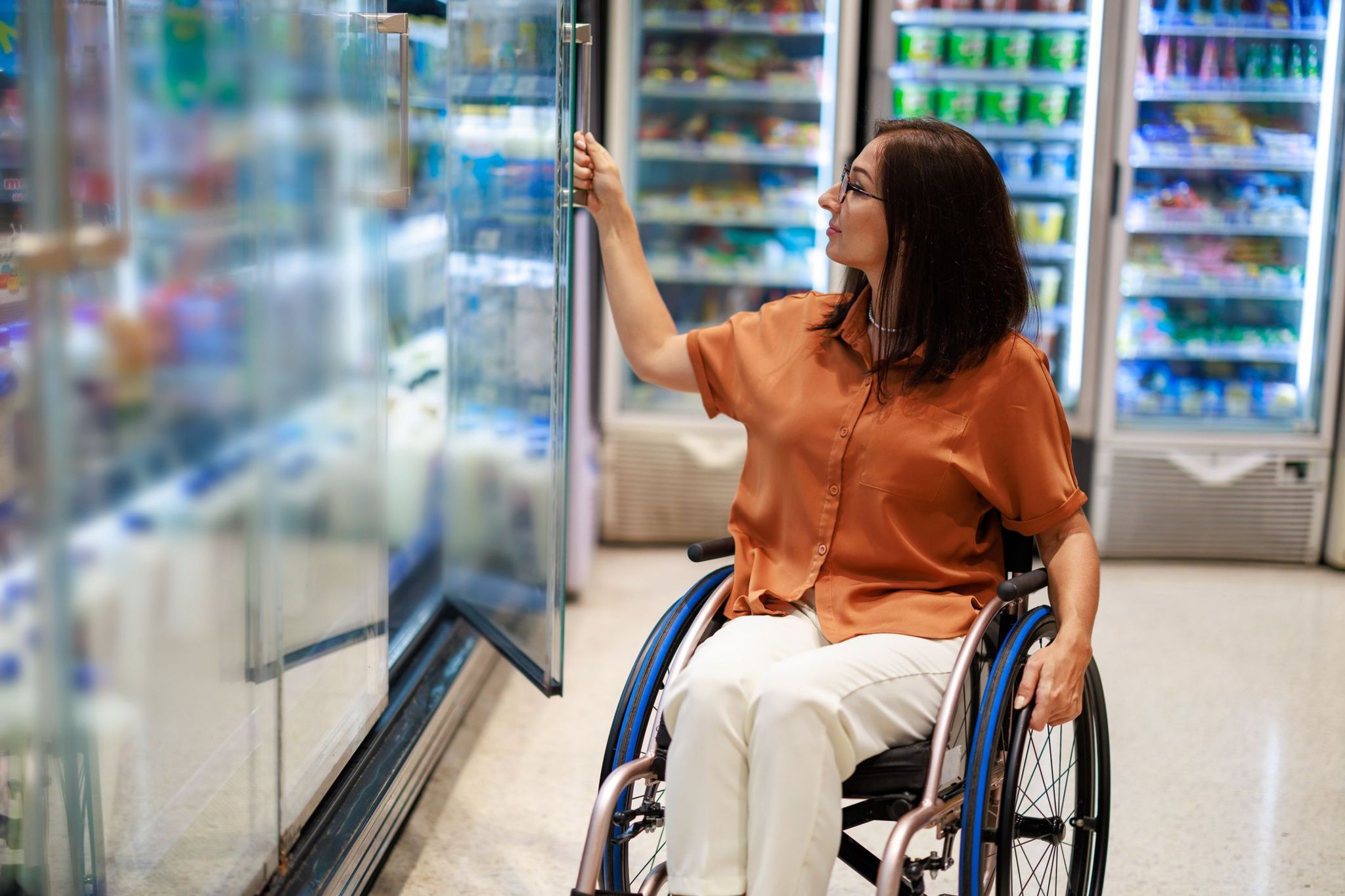 A woman in a wheelchair opens a fridge door in a supermarket