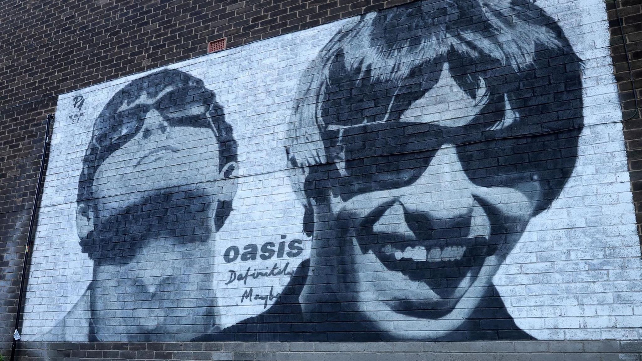 An Oasis mural on a brick wall featuring black-and-white portrayals of Noel and Liam Gallagher