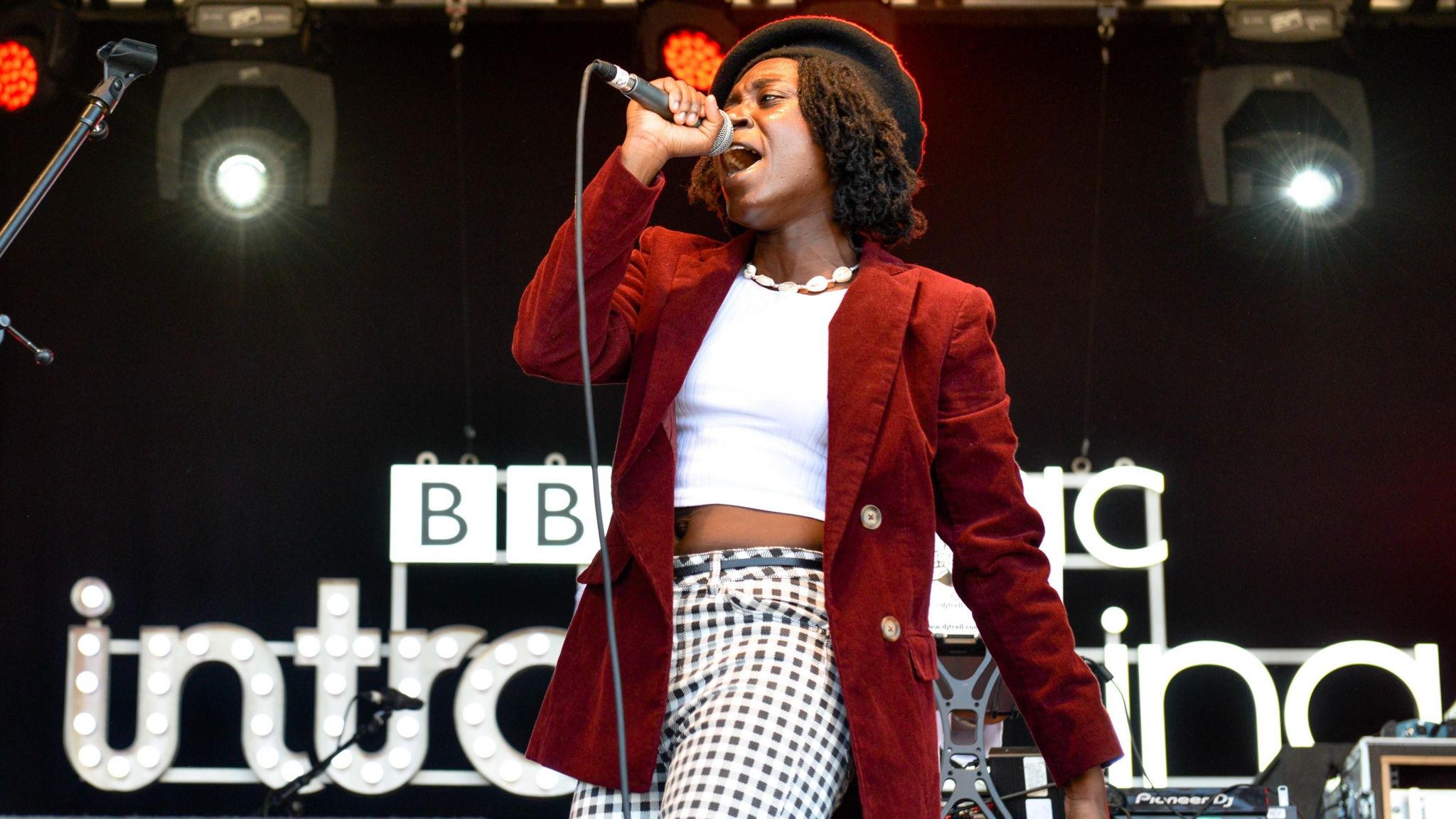 Lavz performing on stage at Reading festival with a read coat and black and white patterned trousers