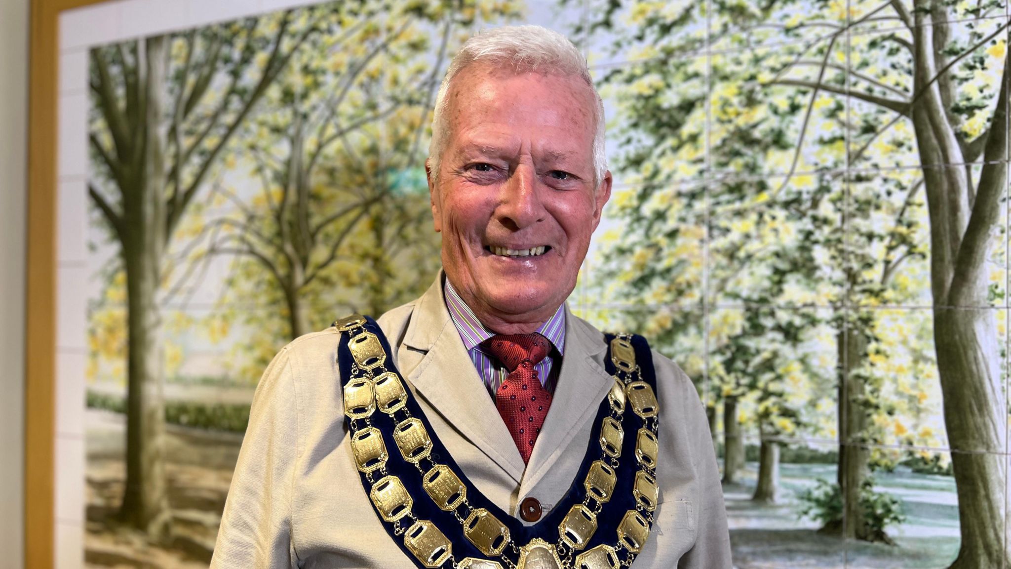 Weston mayor John Crockford Hawley smiling into camera wearing mayoral chain and standing in front of the tiled artwork