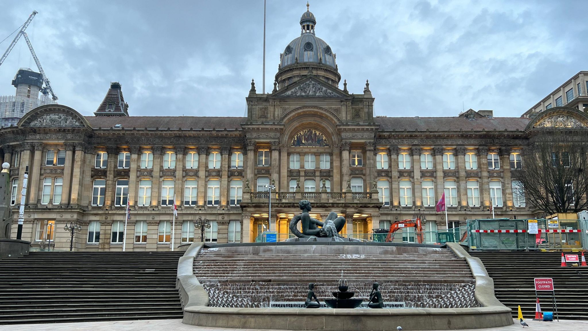 An outside view of Birmingham City Council House in the day with grey clouds above the building and a water fountain in the foreground.
