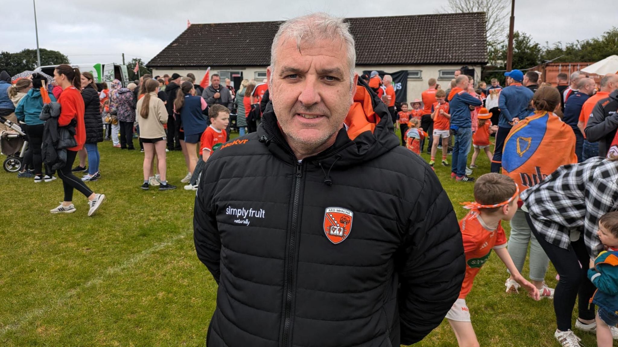 Man standing looking at the camera on a GAA pitch with a crowd of people in the background