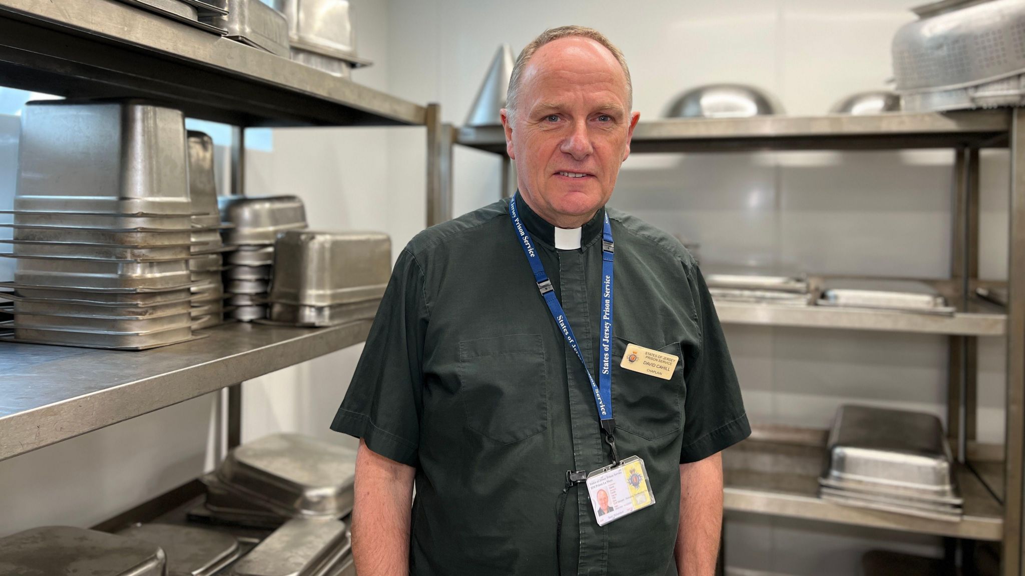 La Moye HMP Chaplain David Cahill stands in the prison kitchen looking at the camera as inmates collect their food for Eid