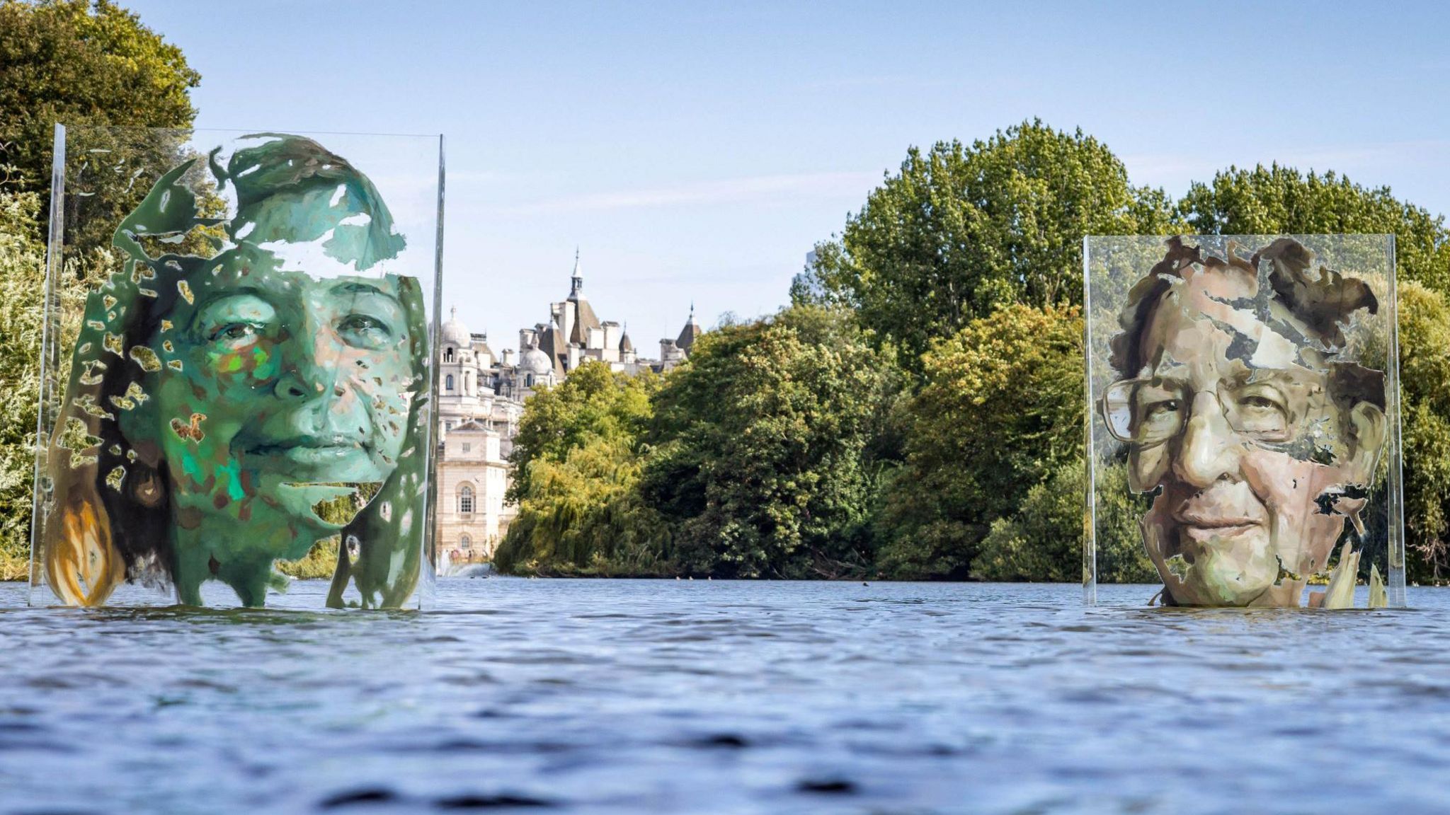 An art installation on a park lake. Two faces on clear Perspex screens appear to float on the water.