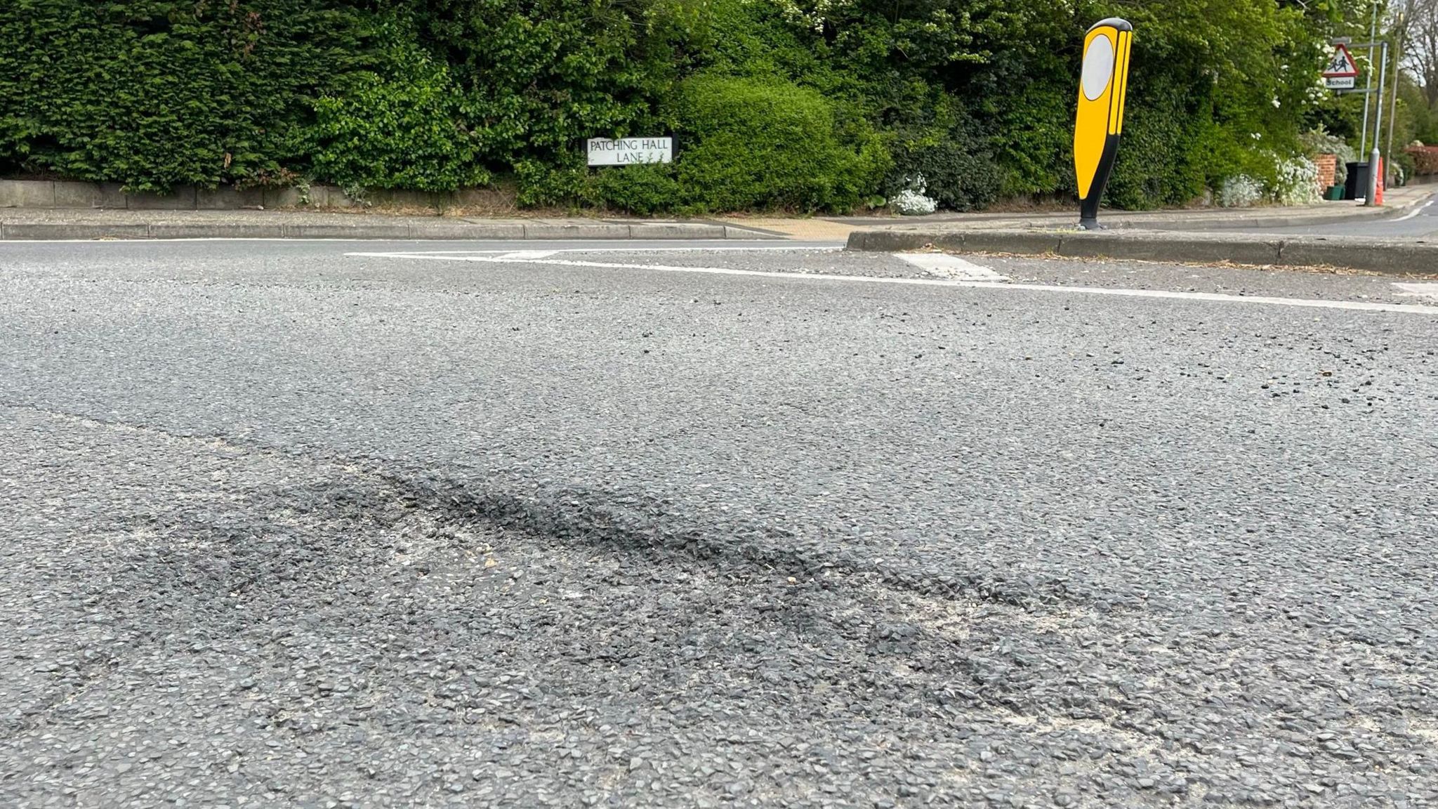 A pothole in the foreground with Patching Hall Lane road sign in the background