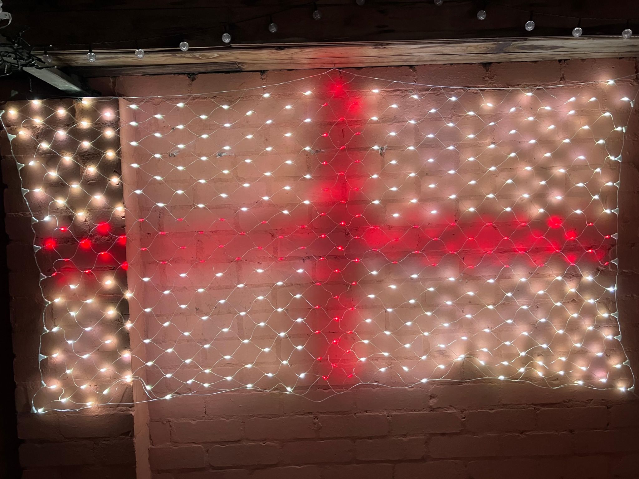 An England flag formed by a net of red and white LEDs hanging on a wall outside a home, captured at night in Halesowen