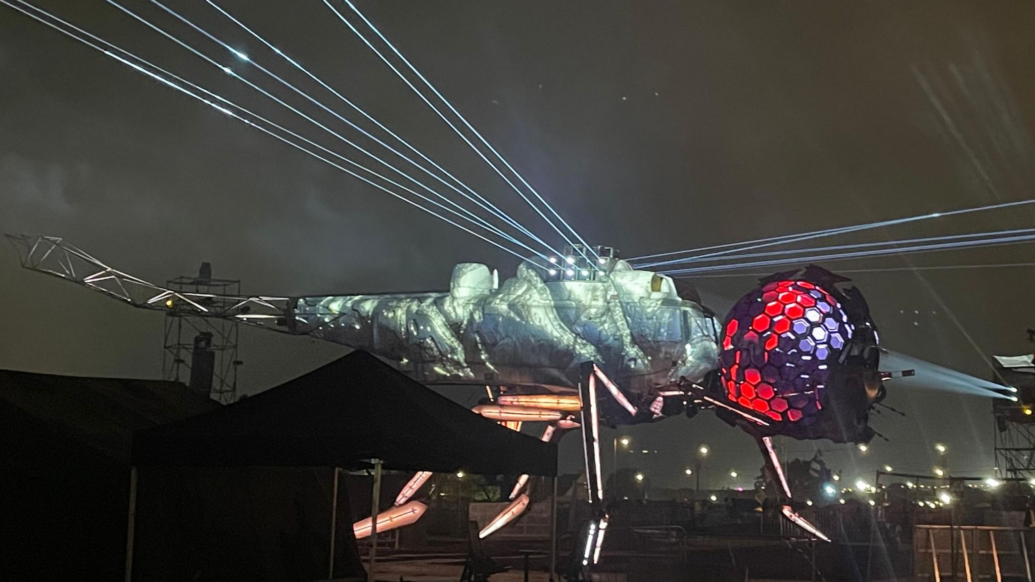 The mechanical Dragonfly sculpture lit-up at night in silver and red colours.