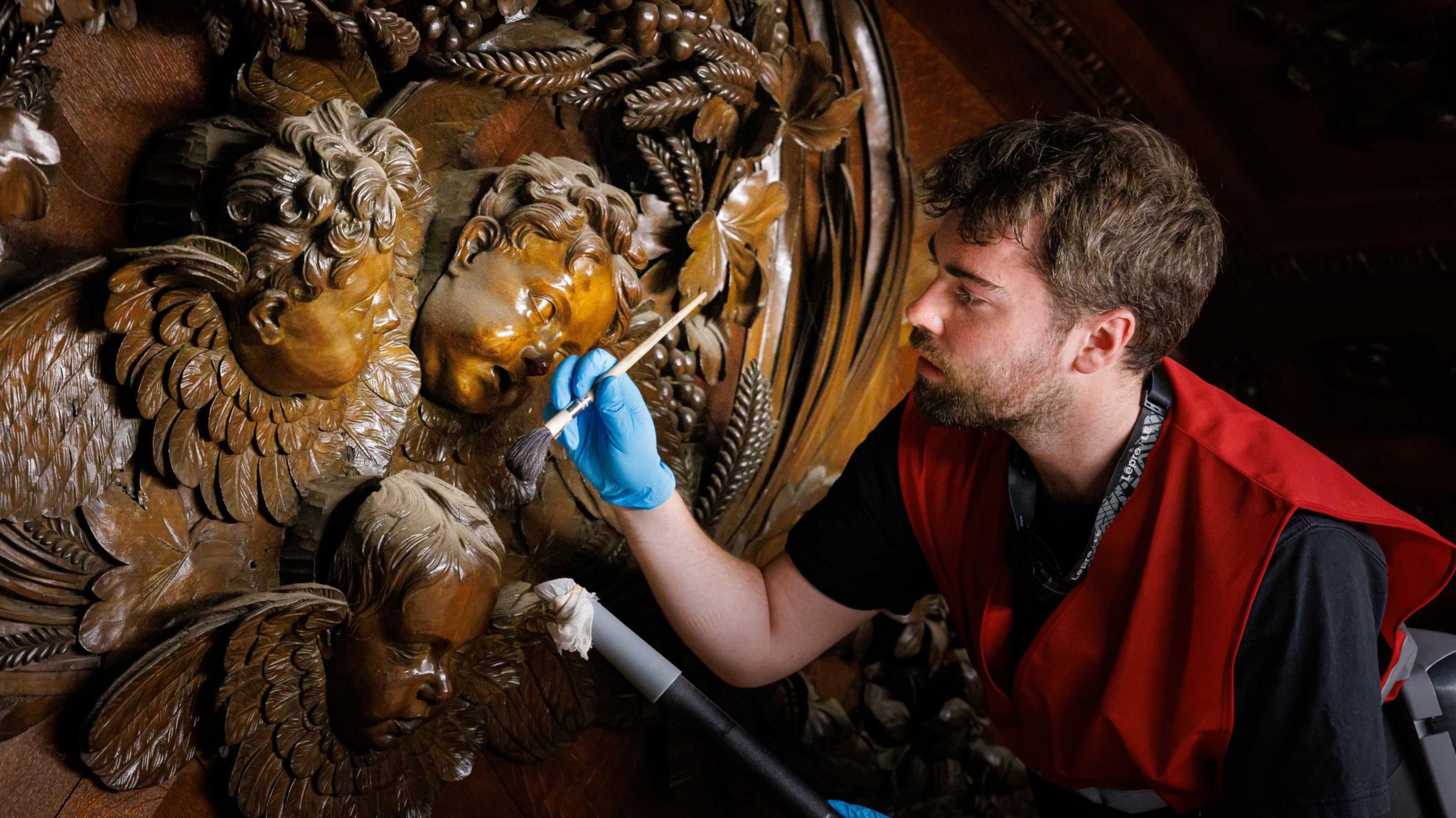 A curator examines a carving of three cherubs at Hampton Court 