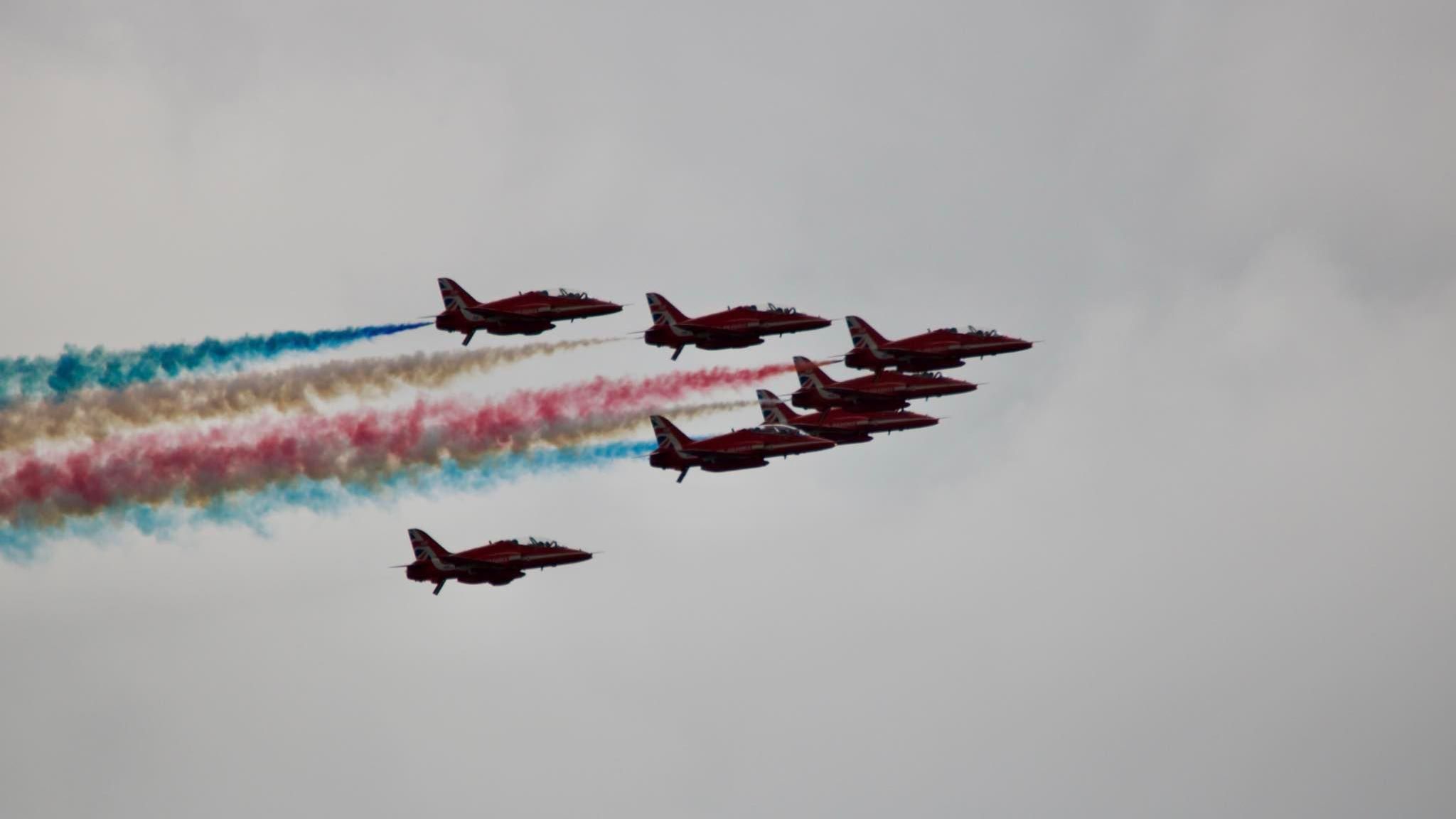 Seven red arrows flying in formation, spouting red, blue and white smoke