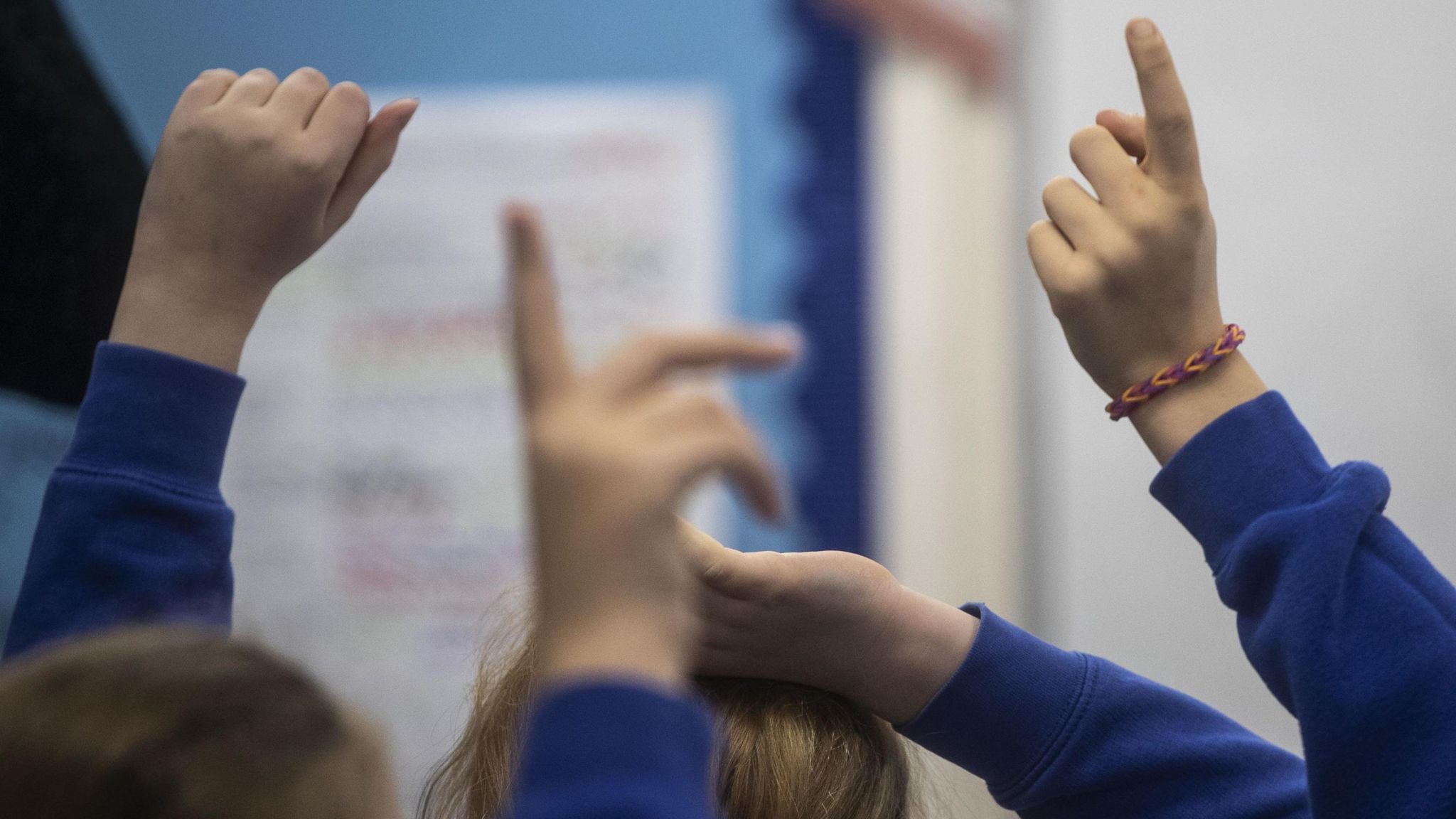 Children with their hands up in a classroom.