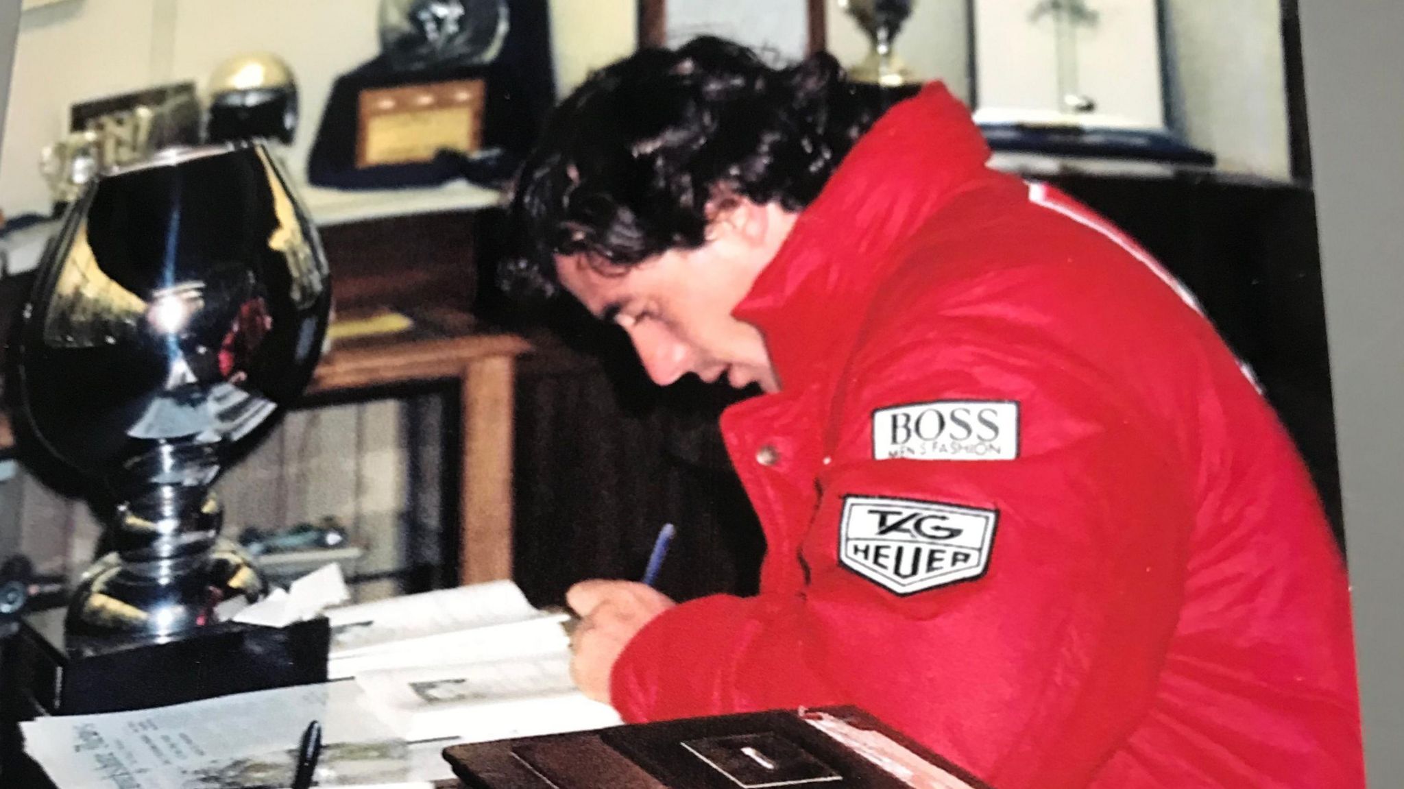 Ayrton Senna dressed in a red McLaren team coat signs the visitor book at the Jim Clark Museum