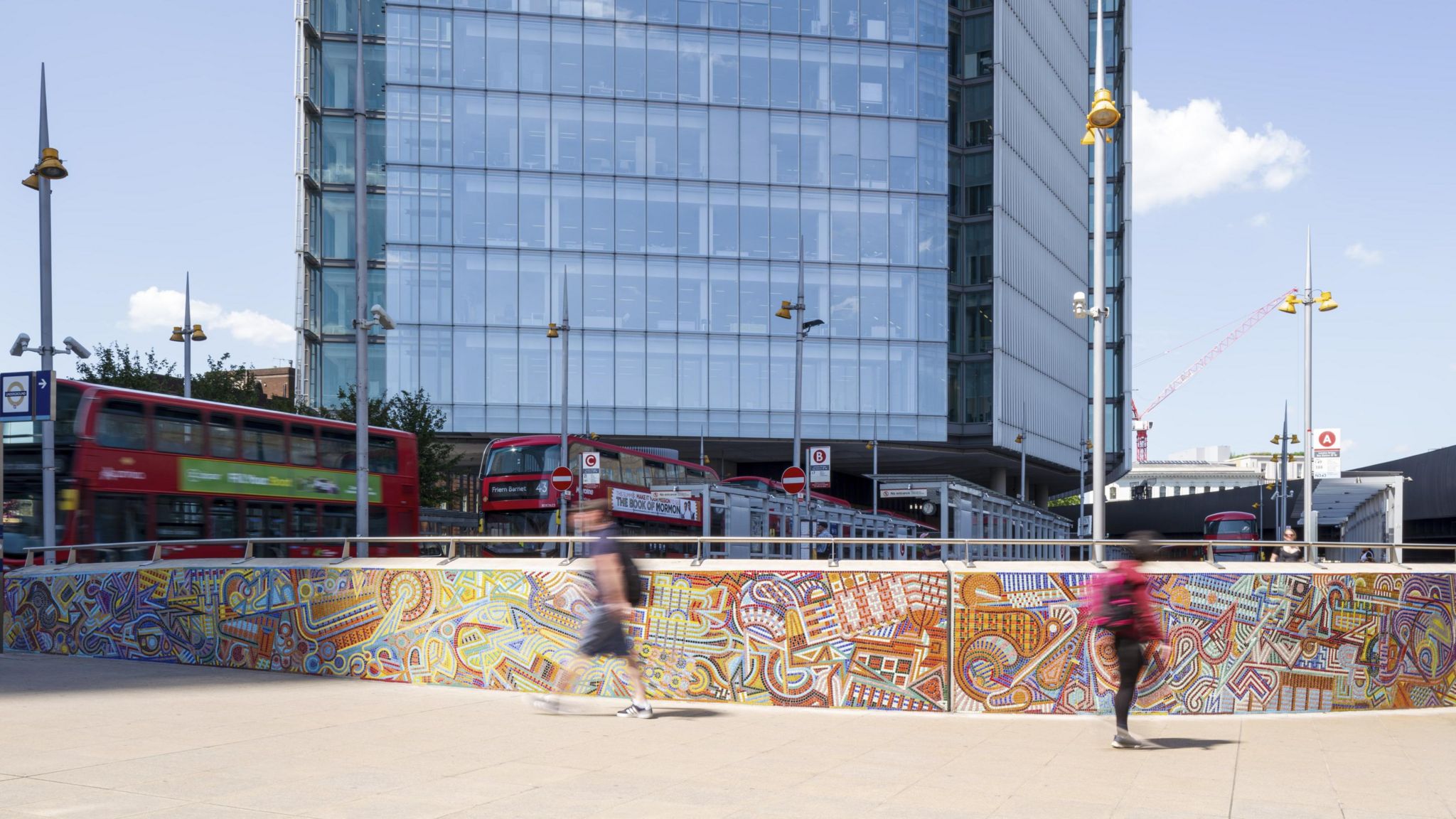 Two people walking past the mural with London buses in the background