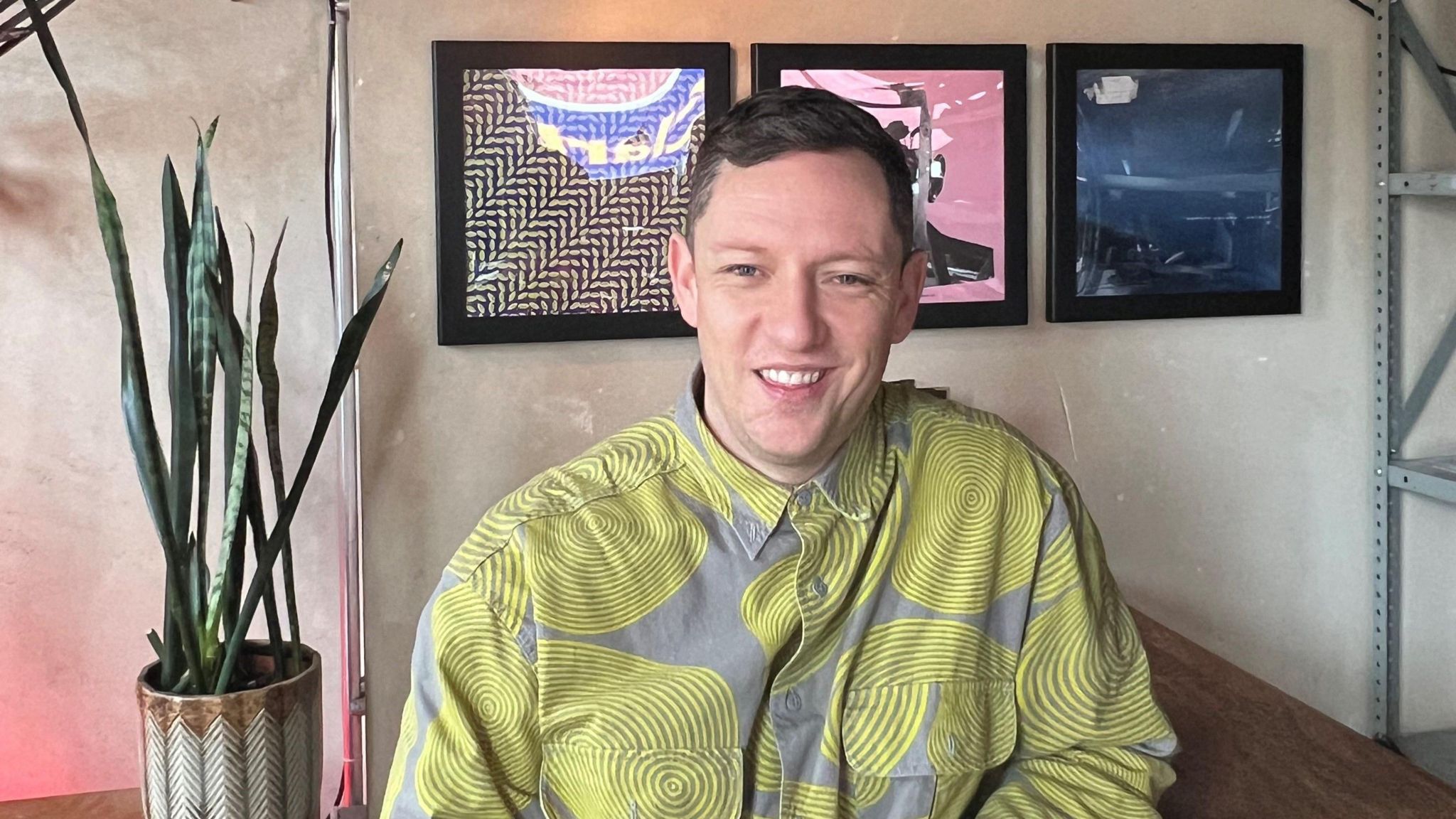 Simple Things director Tom Frost in a grey and yellow shirt, sitting near a plant