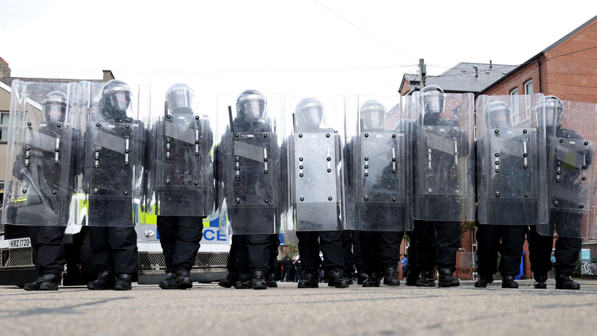 Police in riot gear with shields standing in a row