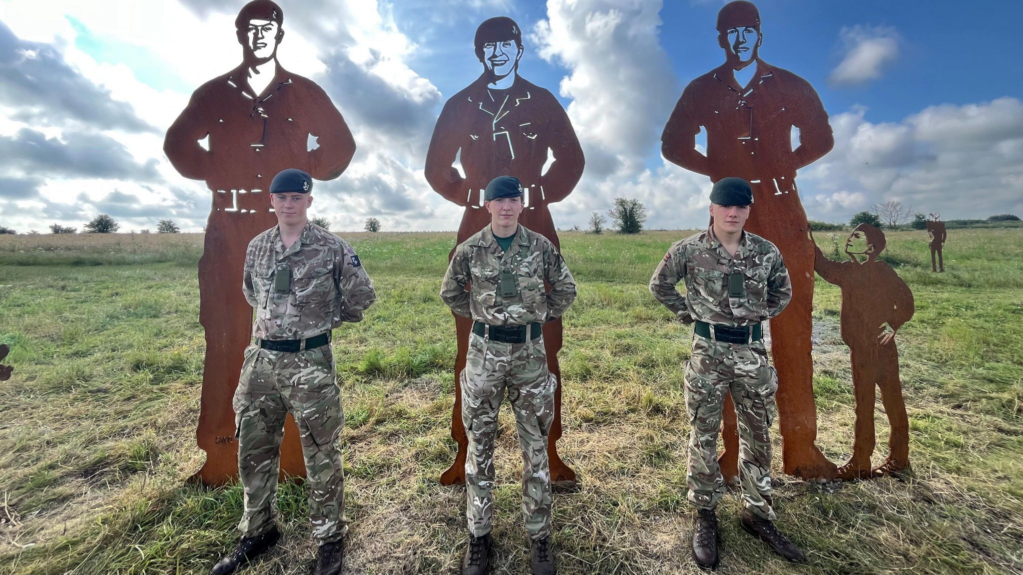 Three soldiers stood in a field in front of the artworks they inspired