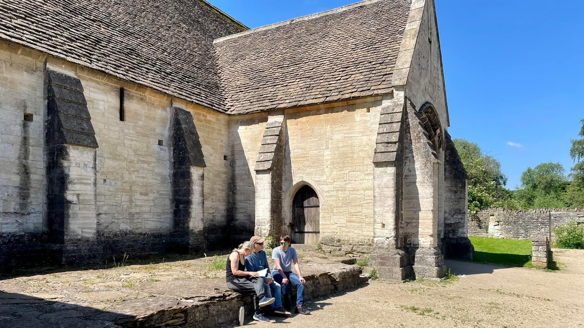 Three people sitting outside of the Tithe Barn during a sunny day 