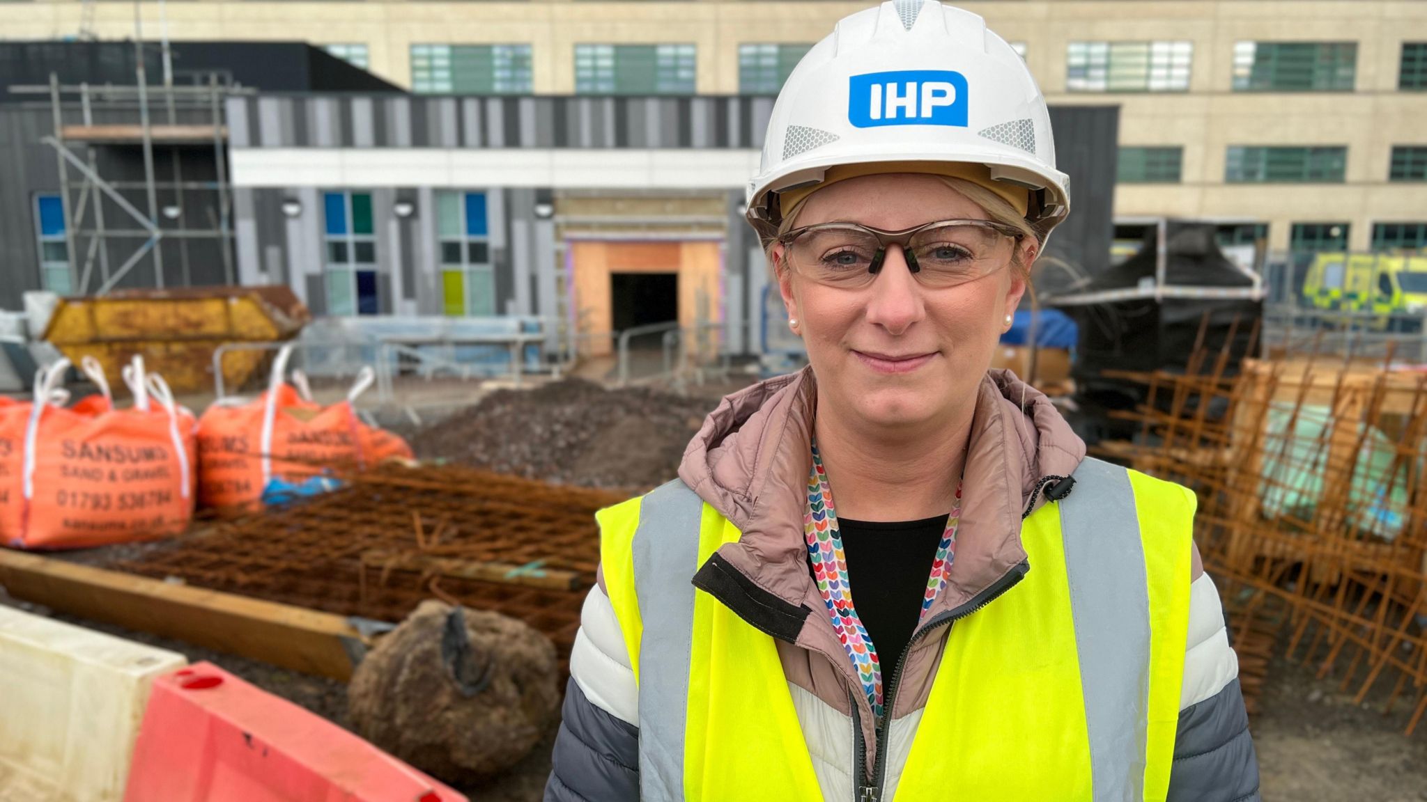 Image of Natalie Lawrence. She is pictured outside the hospital, by the construction. She is wearing a hi-vis vest and a hard hat.