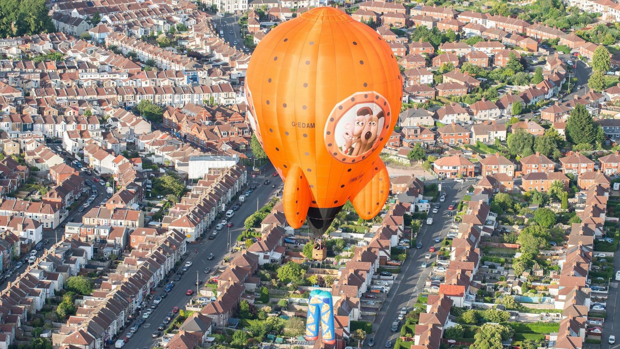 The orange 'Wrong Trousers' hot air balloon flies over houses in Knowle West in Bristol