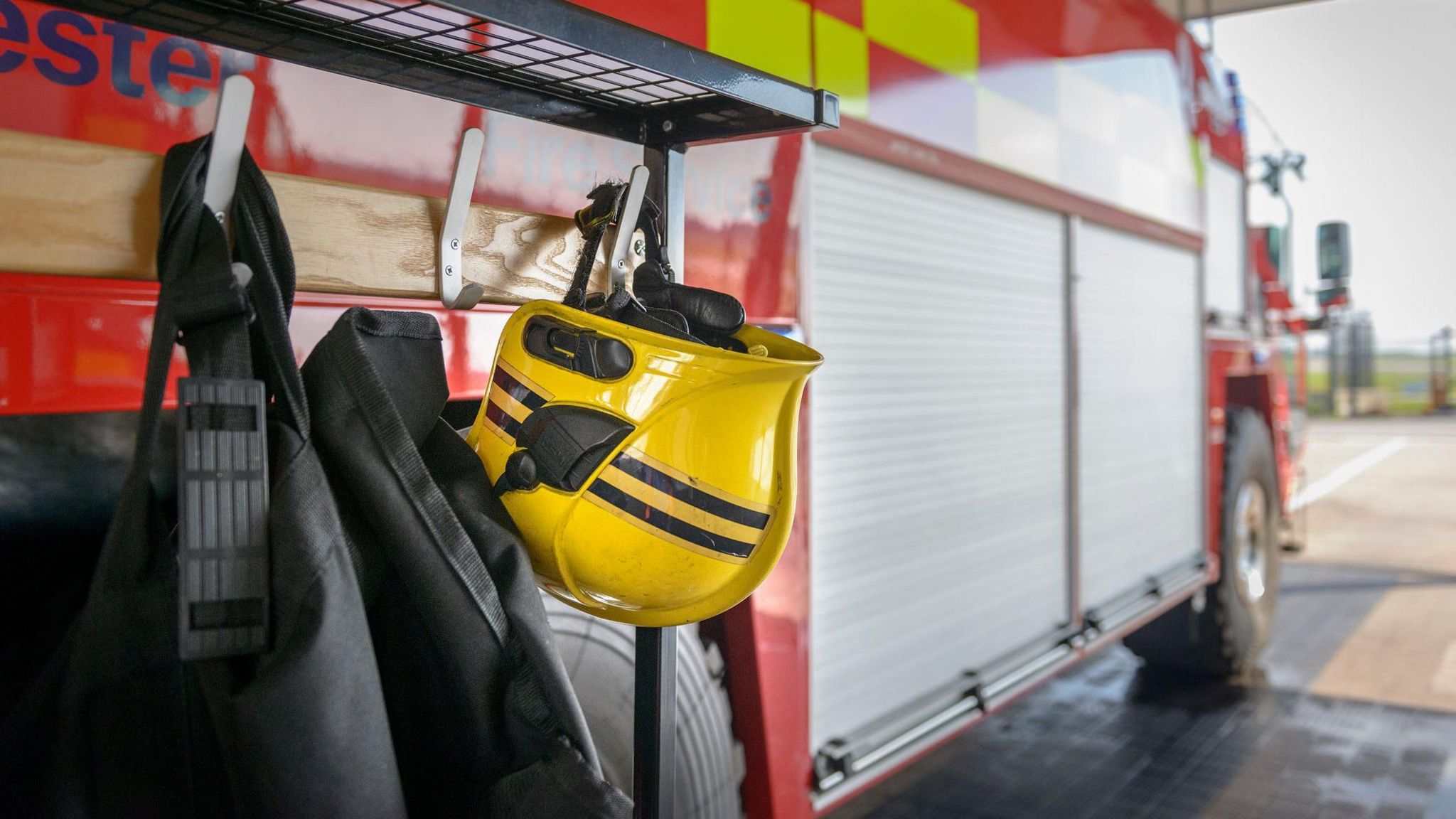 A firefighter's yellow helmet is hung up on the side of a fire engine. 