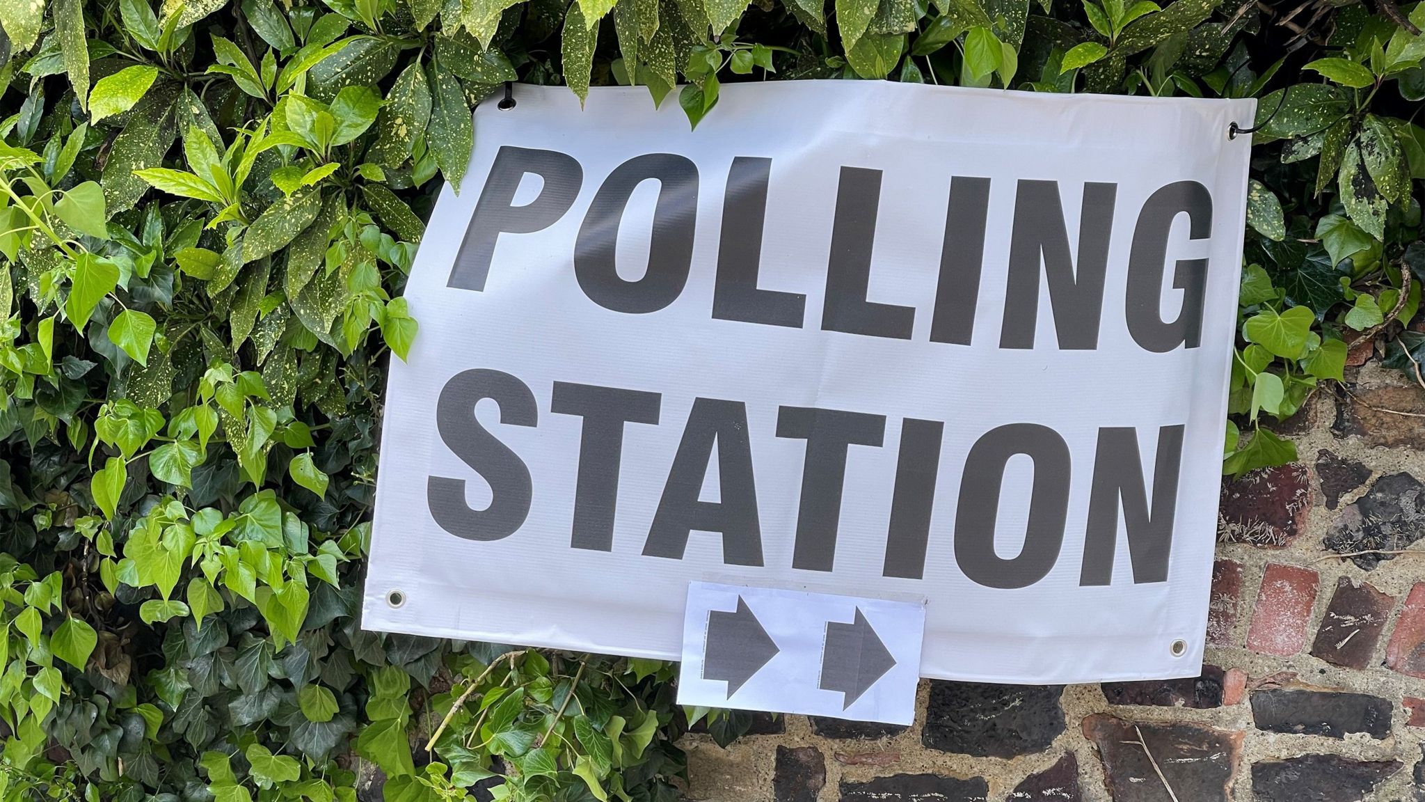 Sign for polling station with accompanying arrows on a brick wall