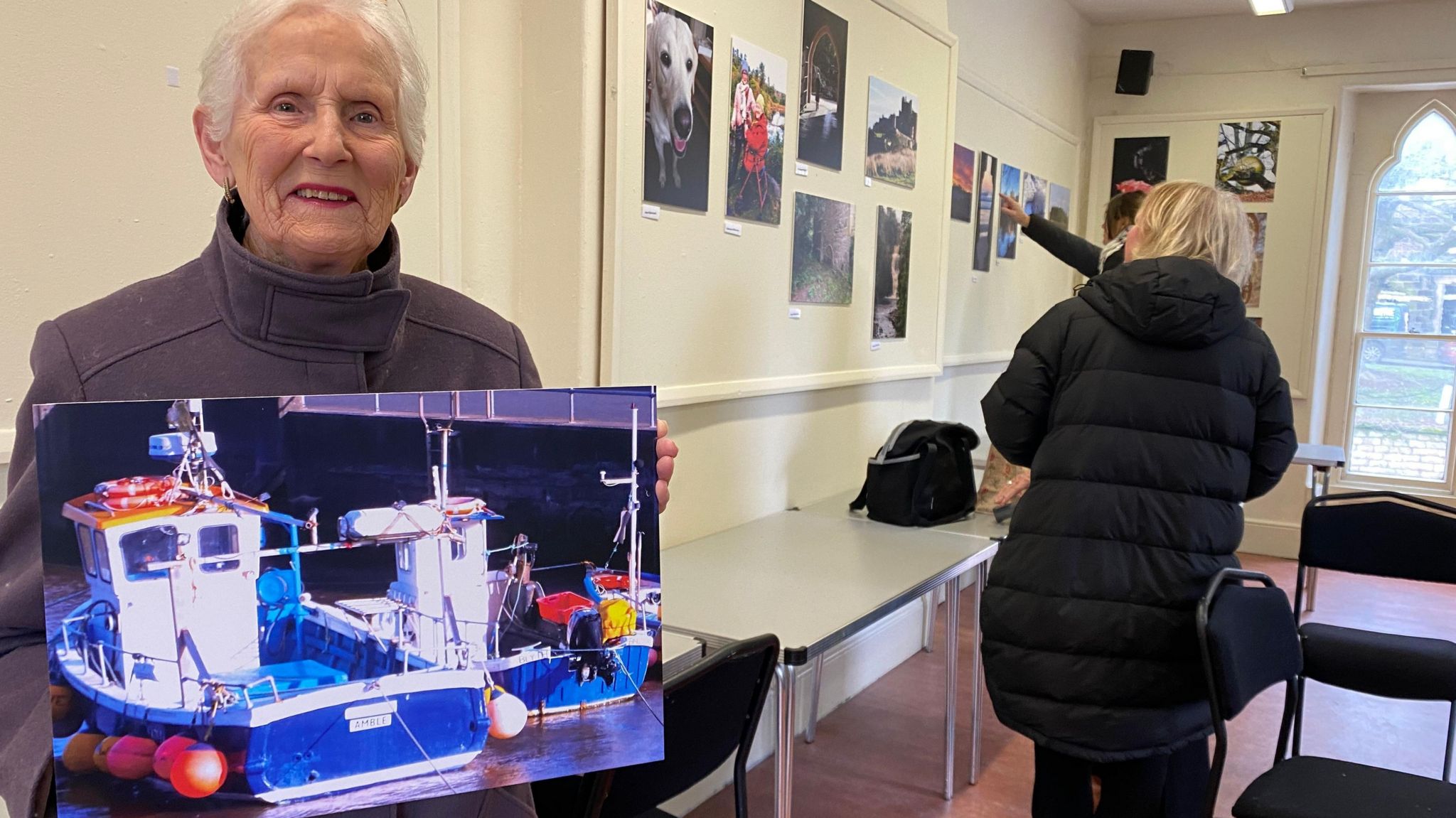 An older lady holds a picture of boats in Amble Harbour in Northumberland 