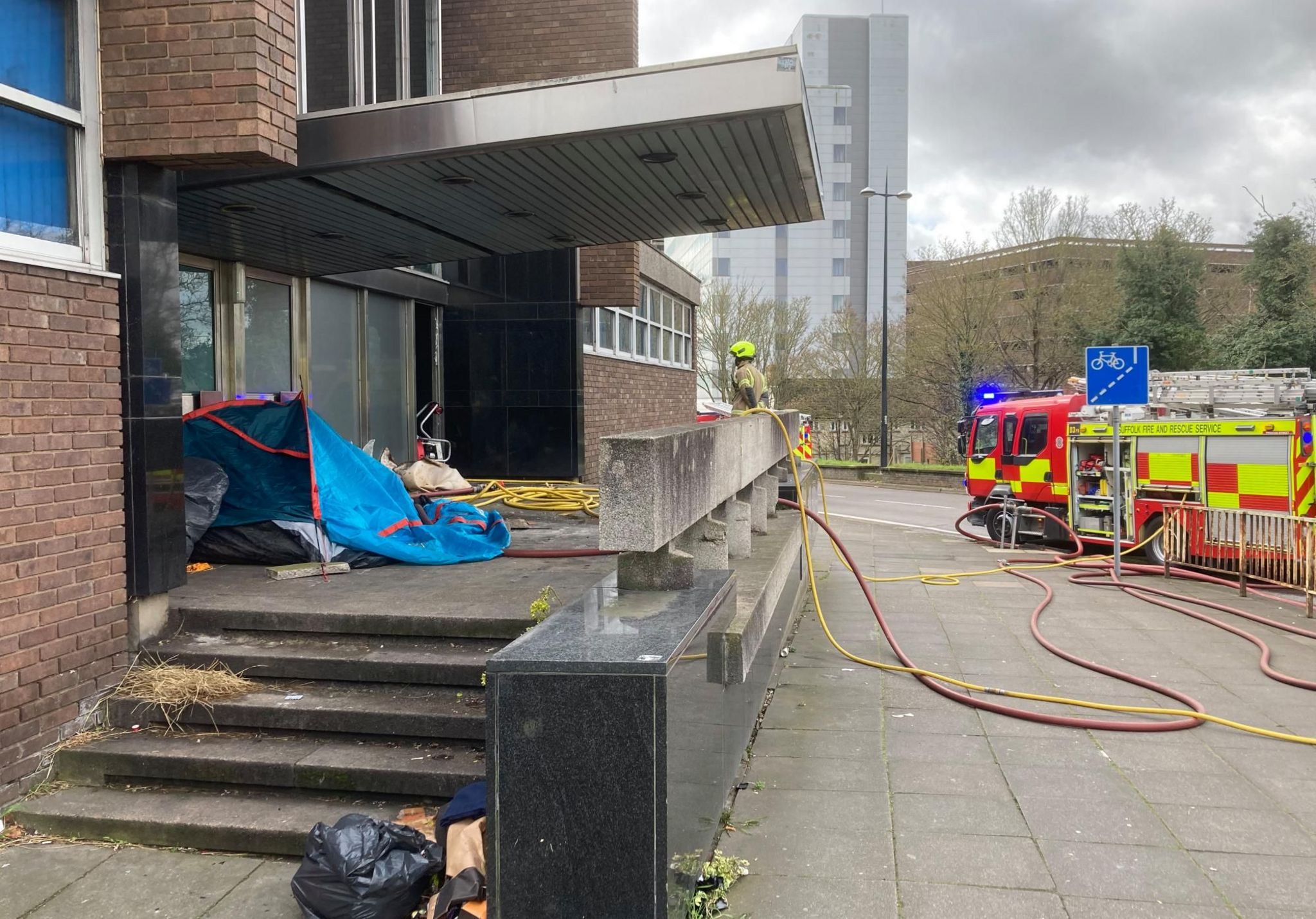 Tent on the steps of Ipswich's former crown court building with fire engines and hoses 
