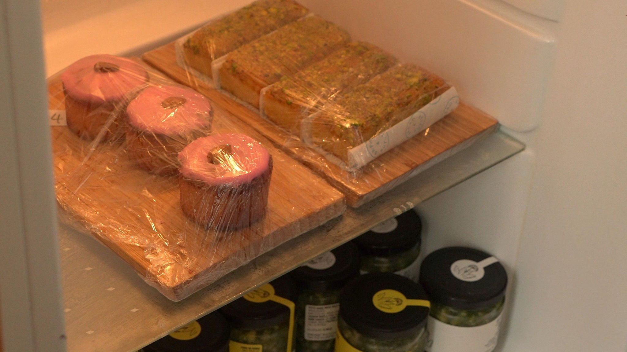 Food in a fridge, including cakes in plastic film and several jars