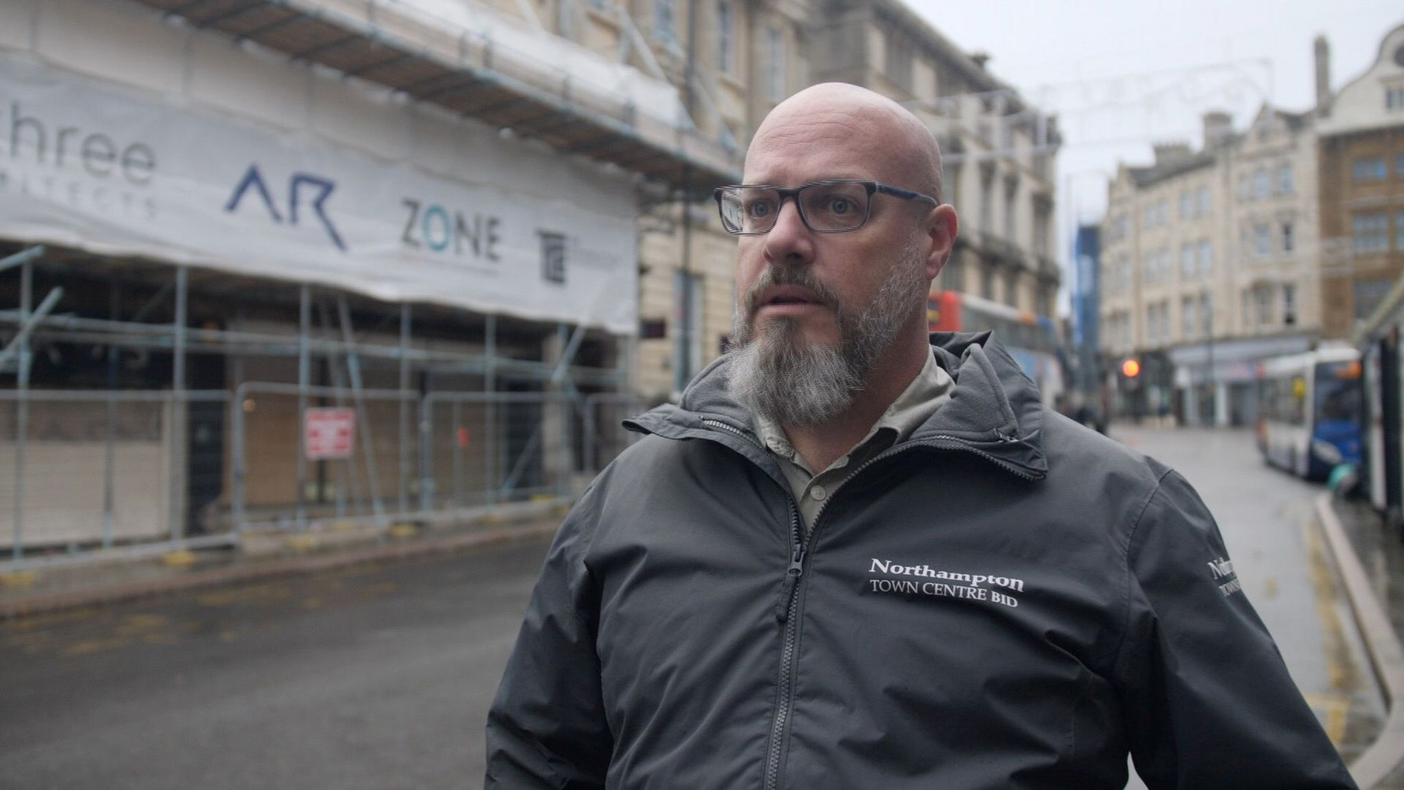 A man in glasses with a long beard stands in front of scaffolding