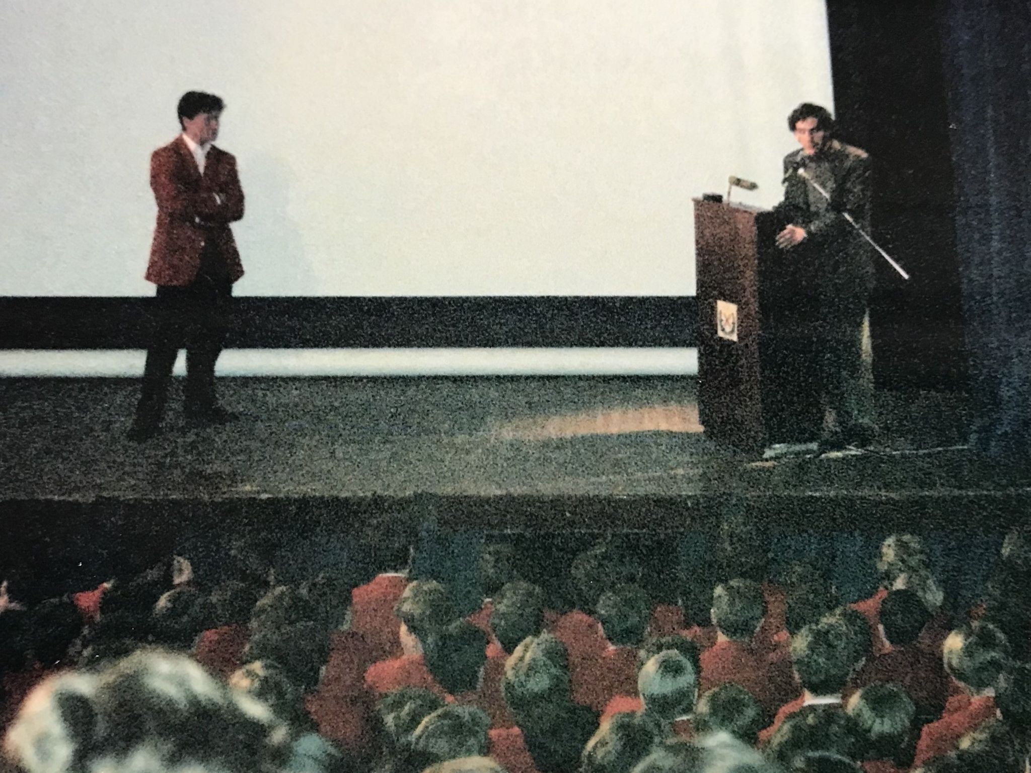 Aryton Senna speaks into a microphone while standing on stage in front of schoolchildren