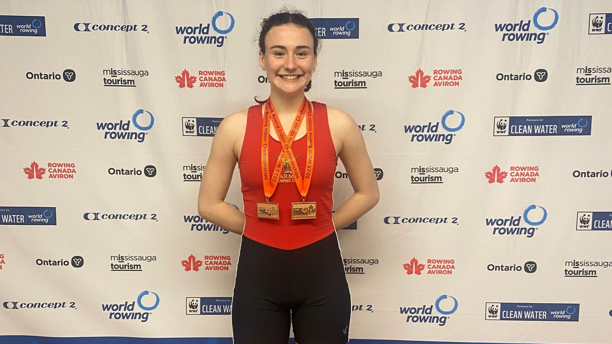 A woman wearing red vest and medals in front of a world rowing championships backdrop