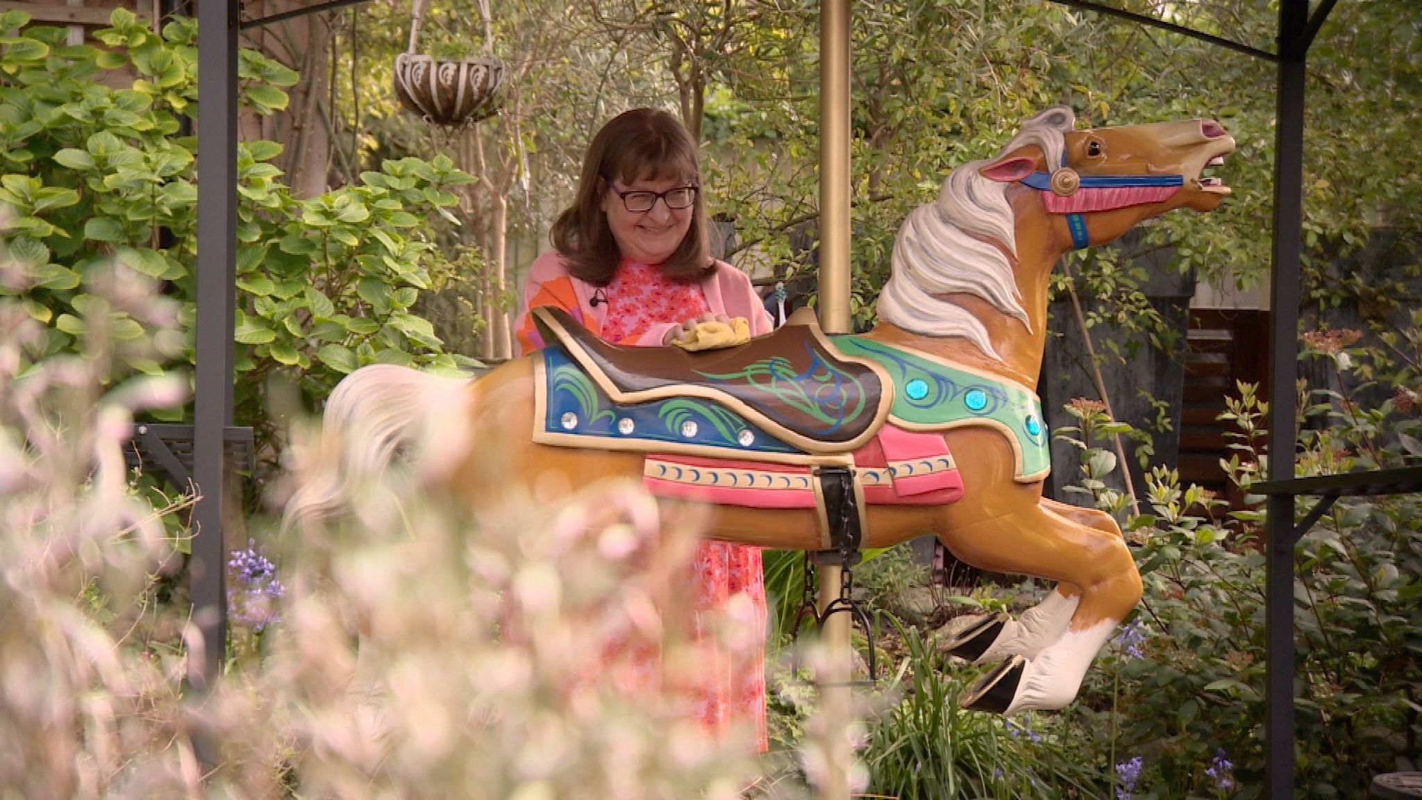 A woman cleans the saddle of a carousel horse in a garden