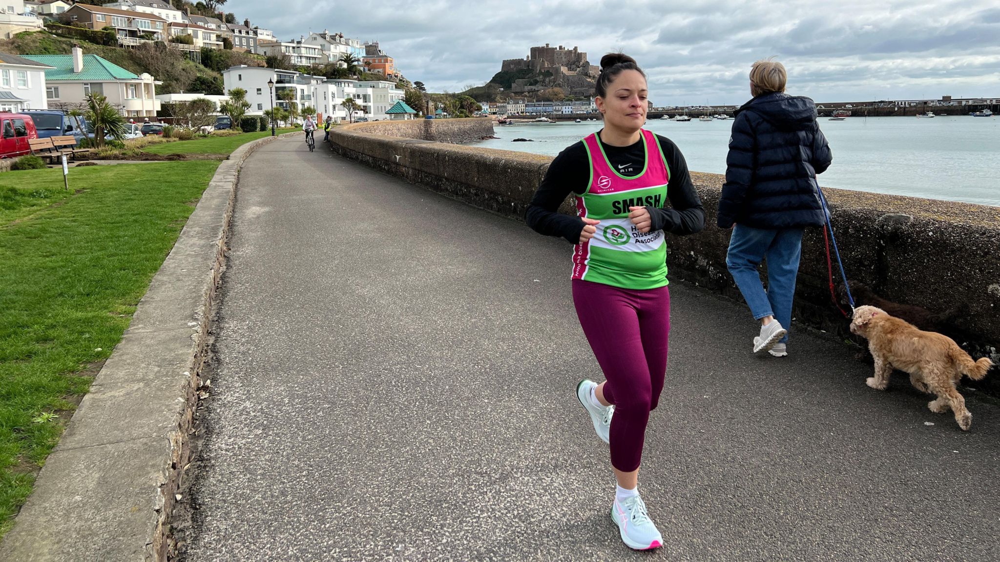 Ashley runs along the coast in Jersey going past a dog walker and there is a castle in the background